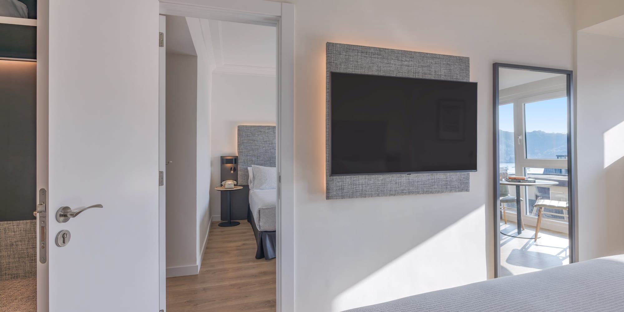 Habitación de hotel moderna con TV, cama y vista al mar reflejada.