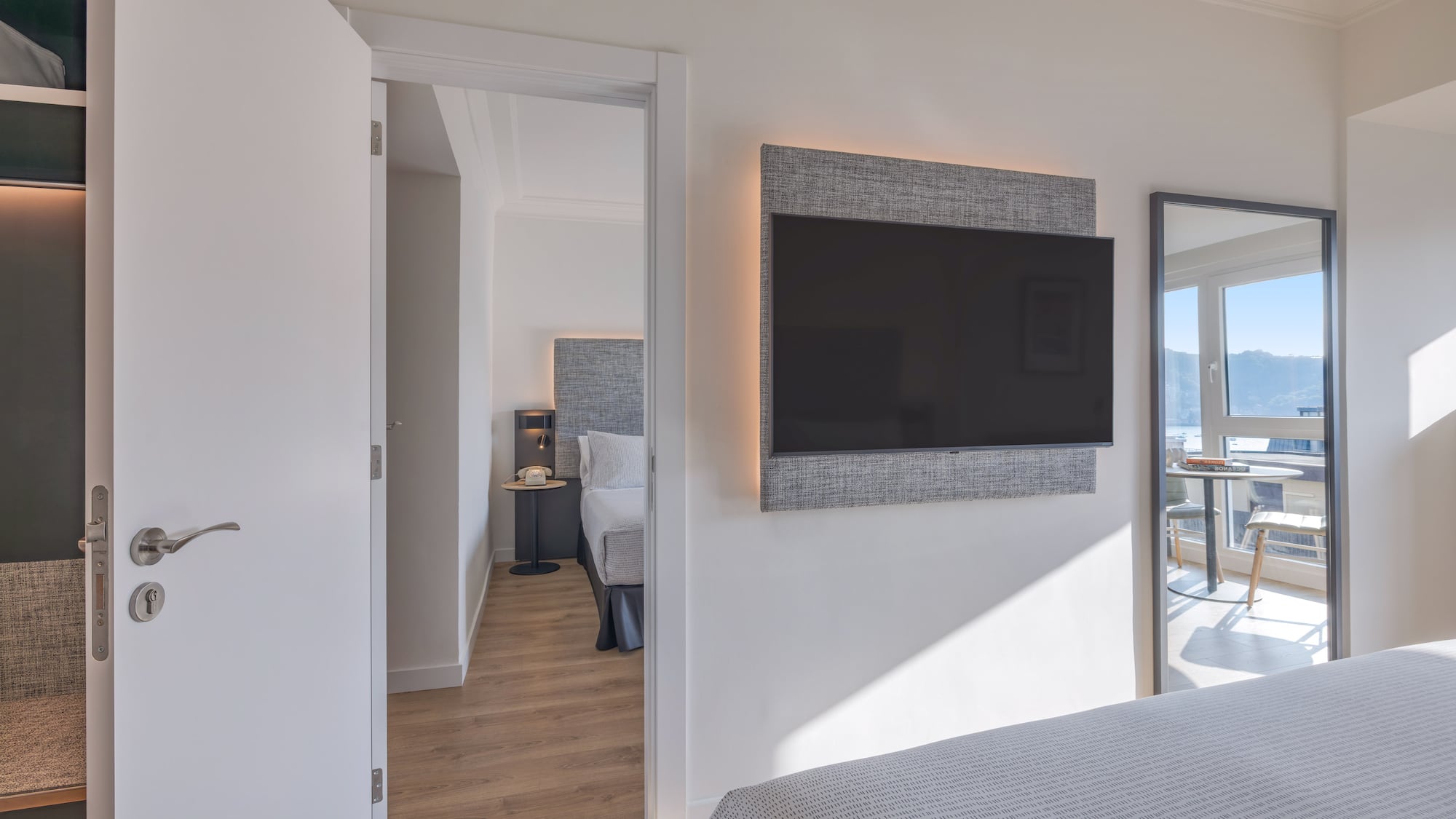 Habitación de hotel moderna con TV, cama y vista al mar reflejada.