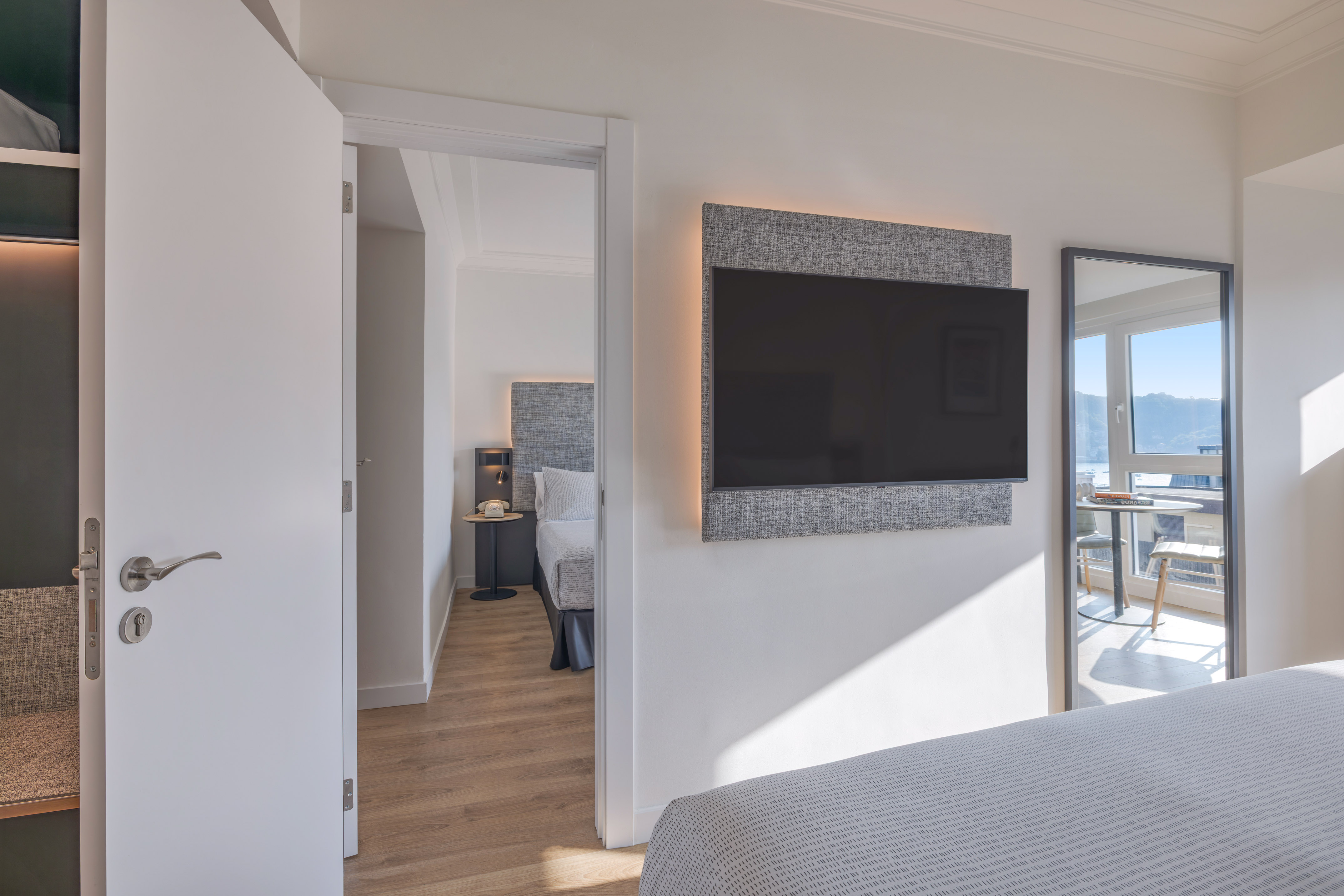 Habitación de hotel moderna con TV, cama y vista al mar reflejada.