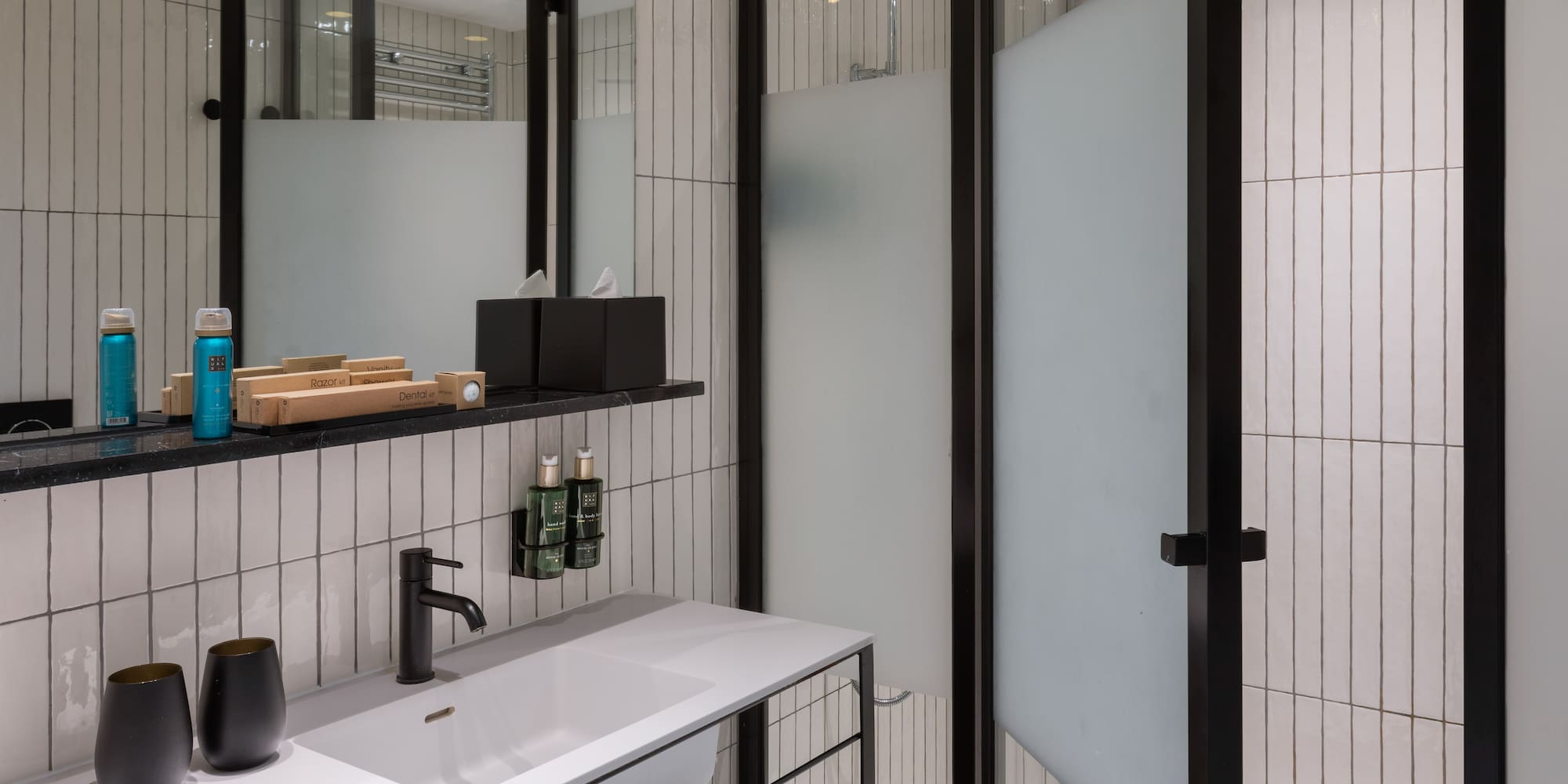Modern bathroom with white tiles, black vanity, sink, mirror, and shower.