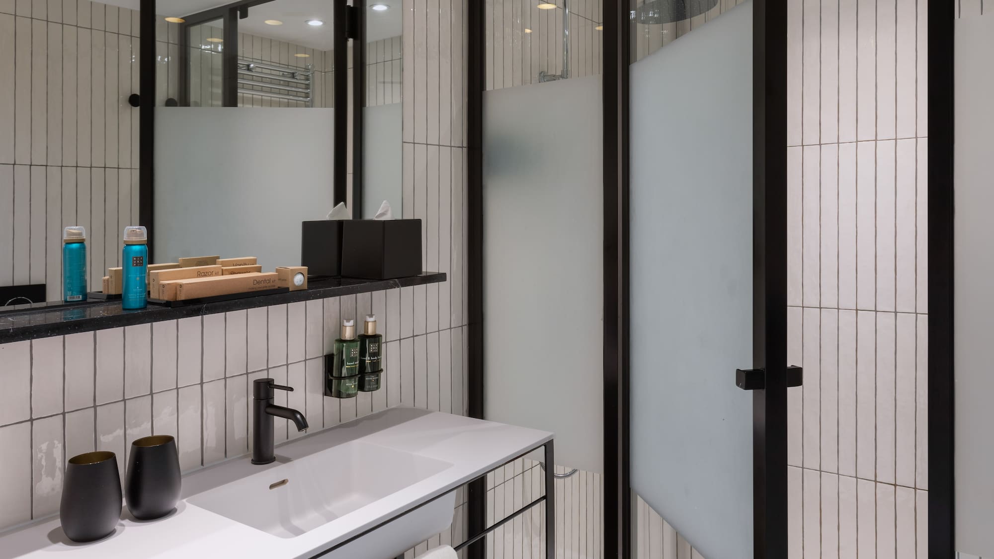 Modern bathroom with white tiles, black vanity, sink, mirror, and shower.