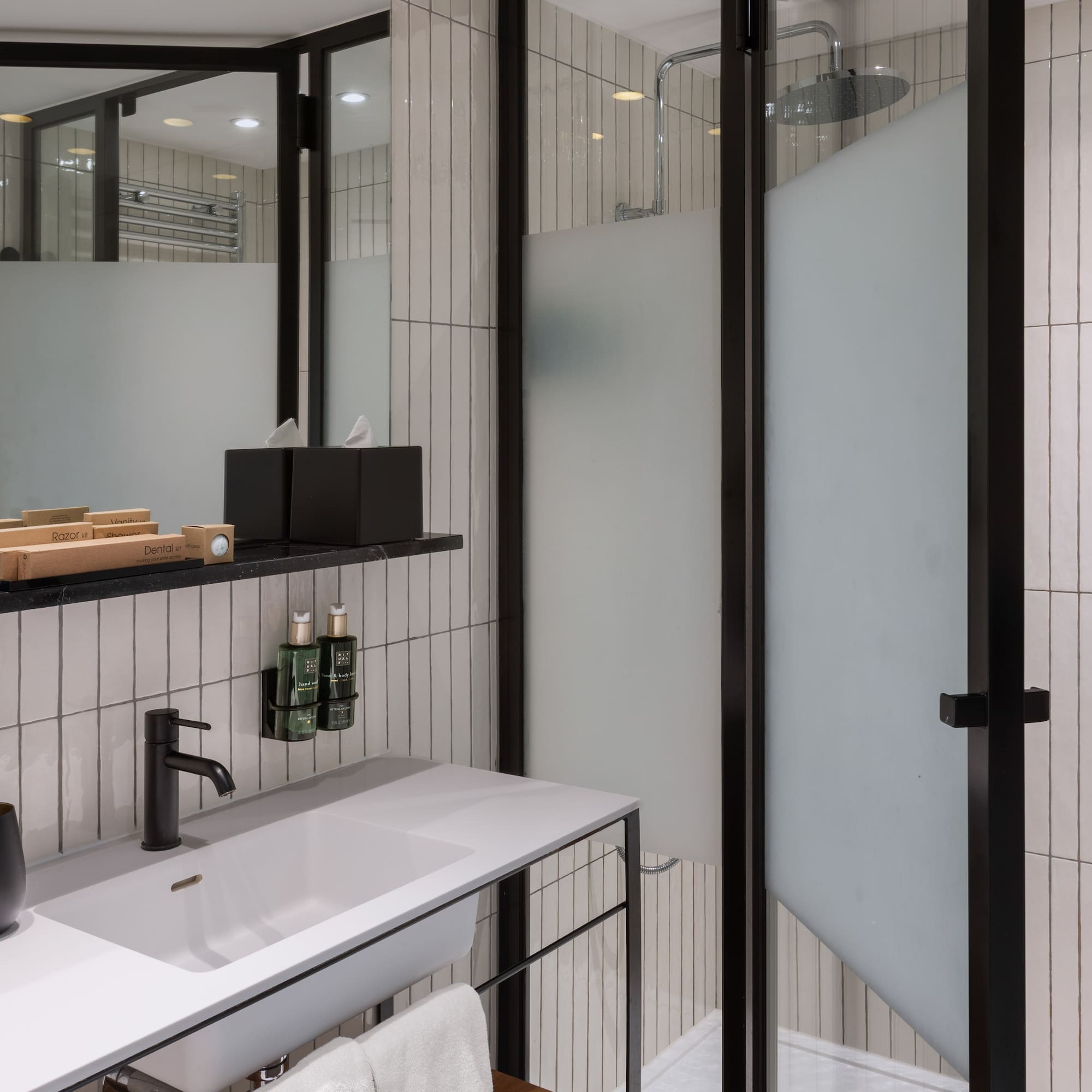 Modern bathroom with white tiles, black vanity, sink, mirror, and shower.