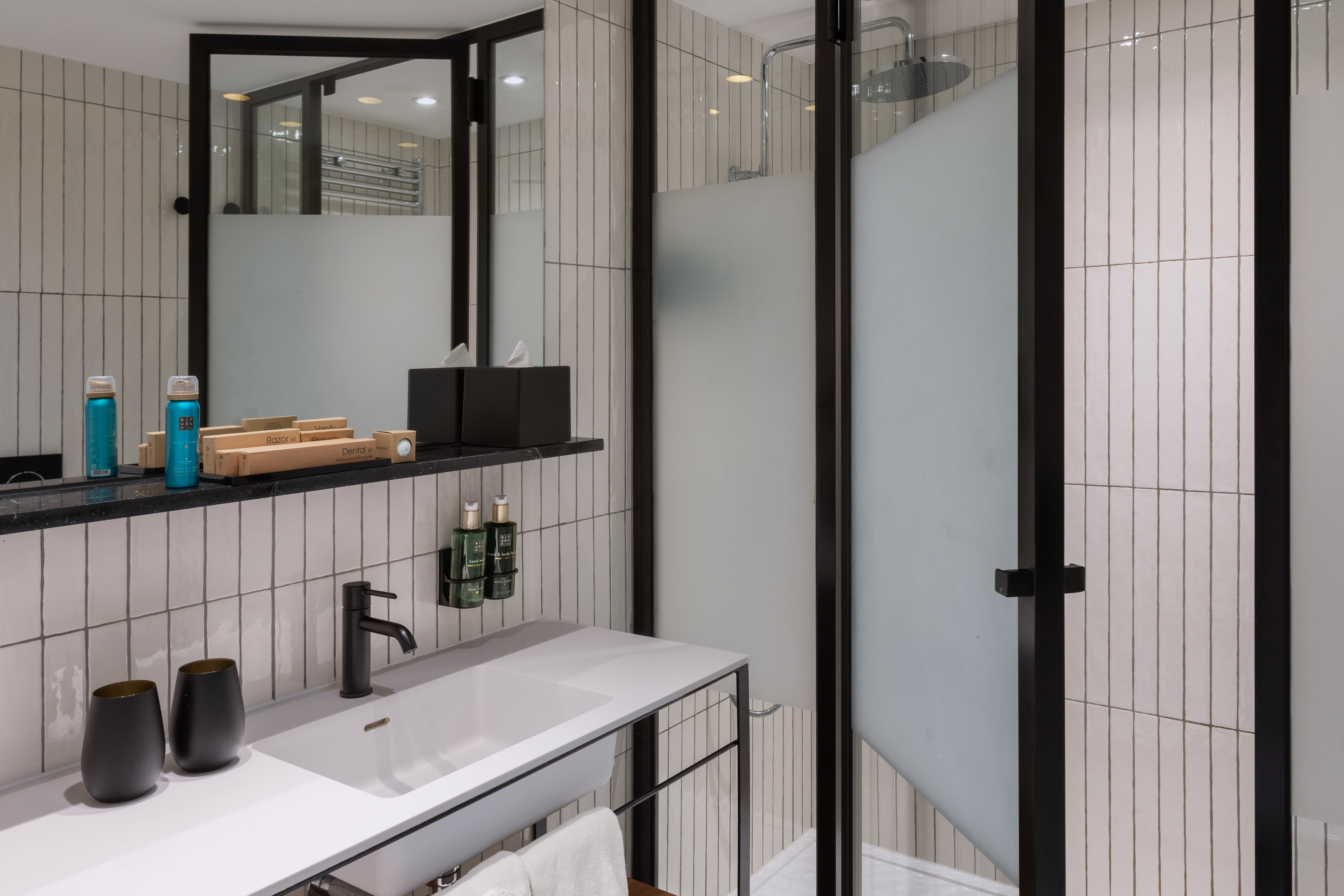 Modern bathroom with white tiles, black vanity, sink, mirror, and shower.