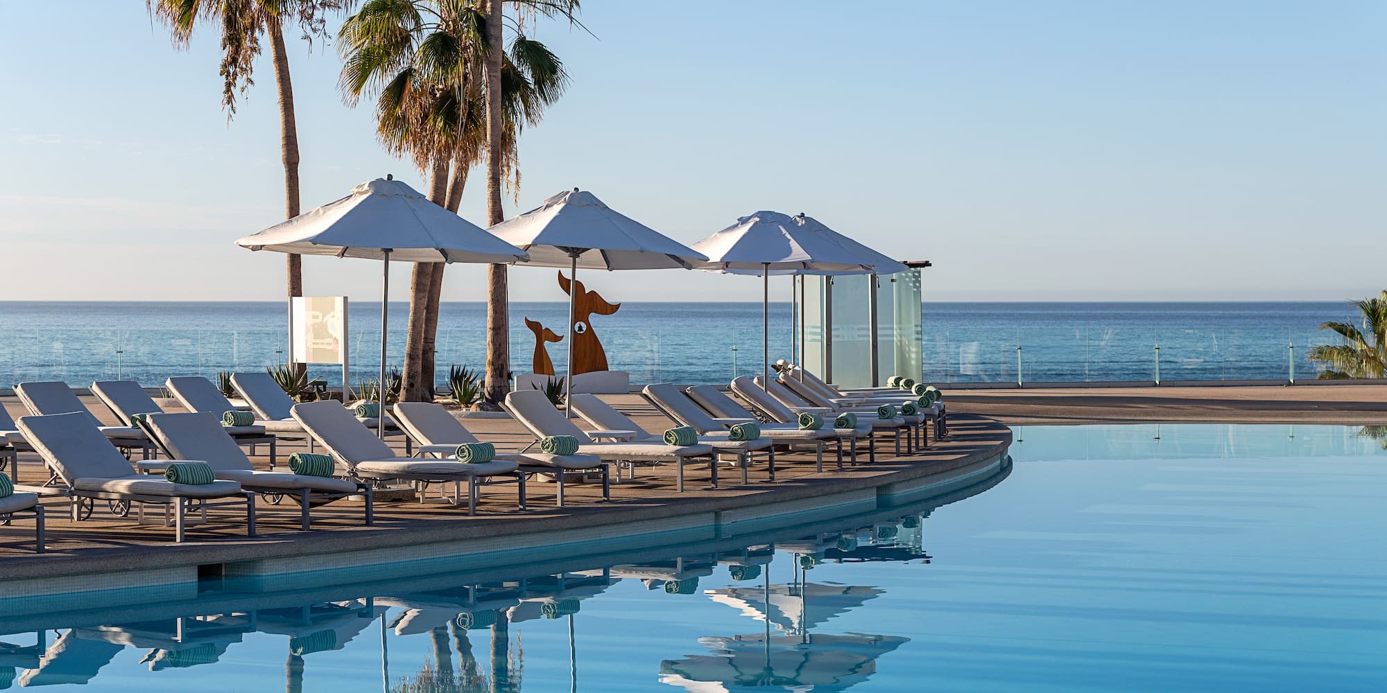 a pool with lounge chairs and umbrellas by the ocean