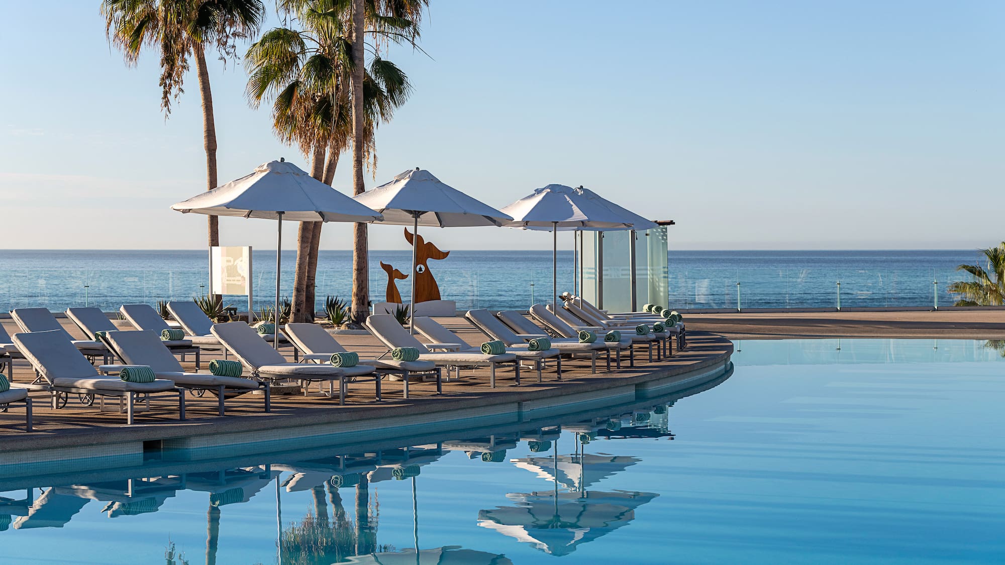 a pool with lounge chairs and umbrellas by the ocean