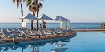 a pool with lounge chairs and umbrellas by the ocean