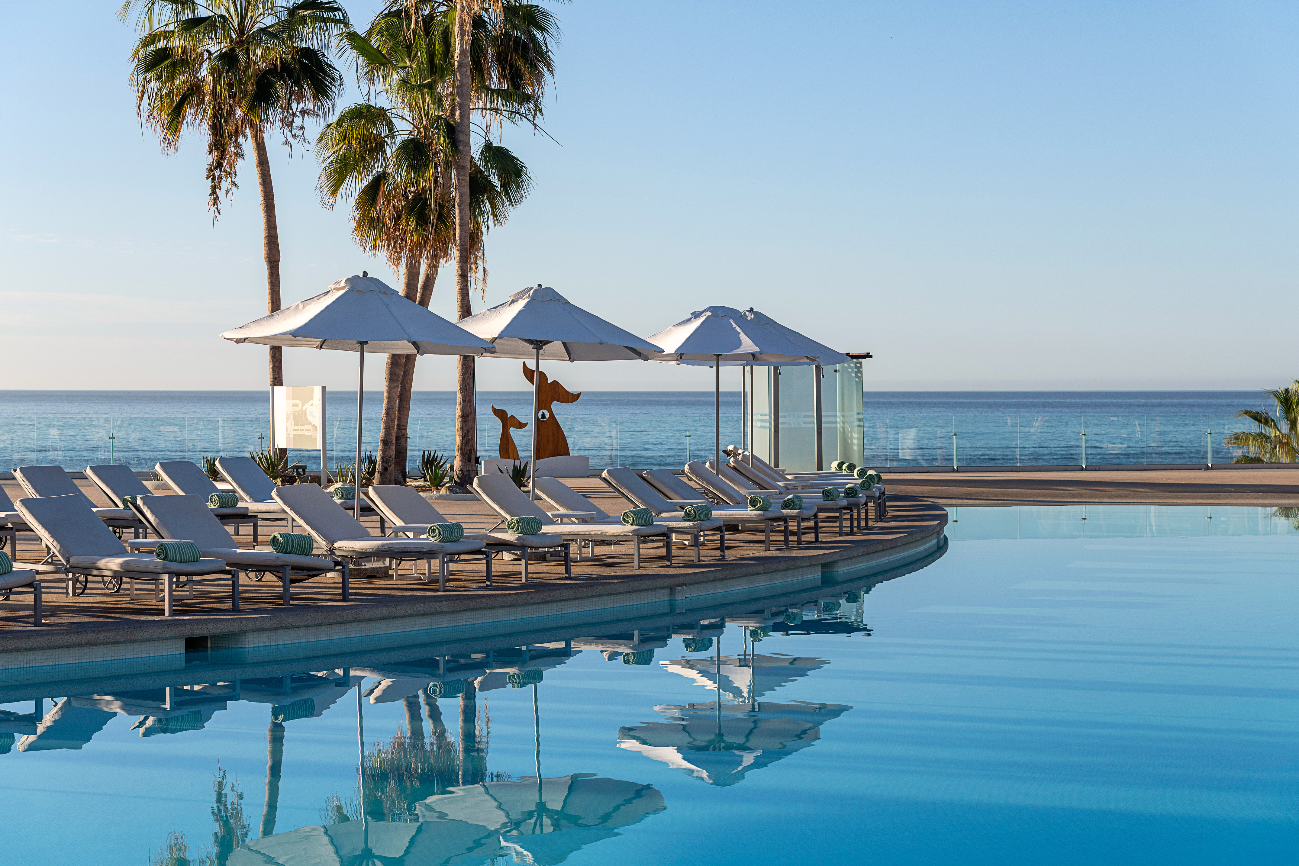 a pool with lounge chairs and umbrellas by the ocean