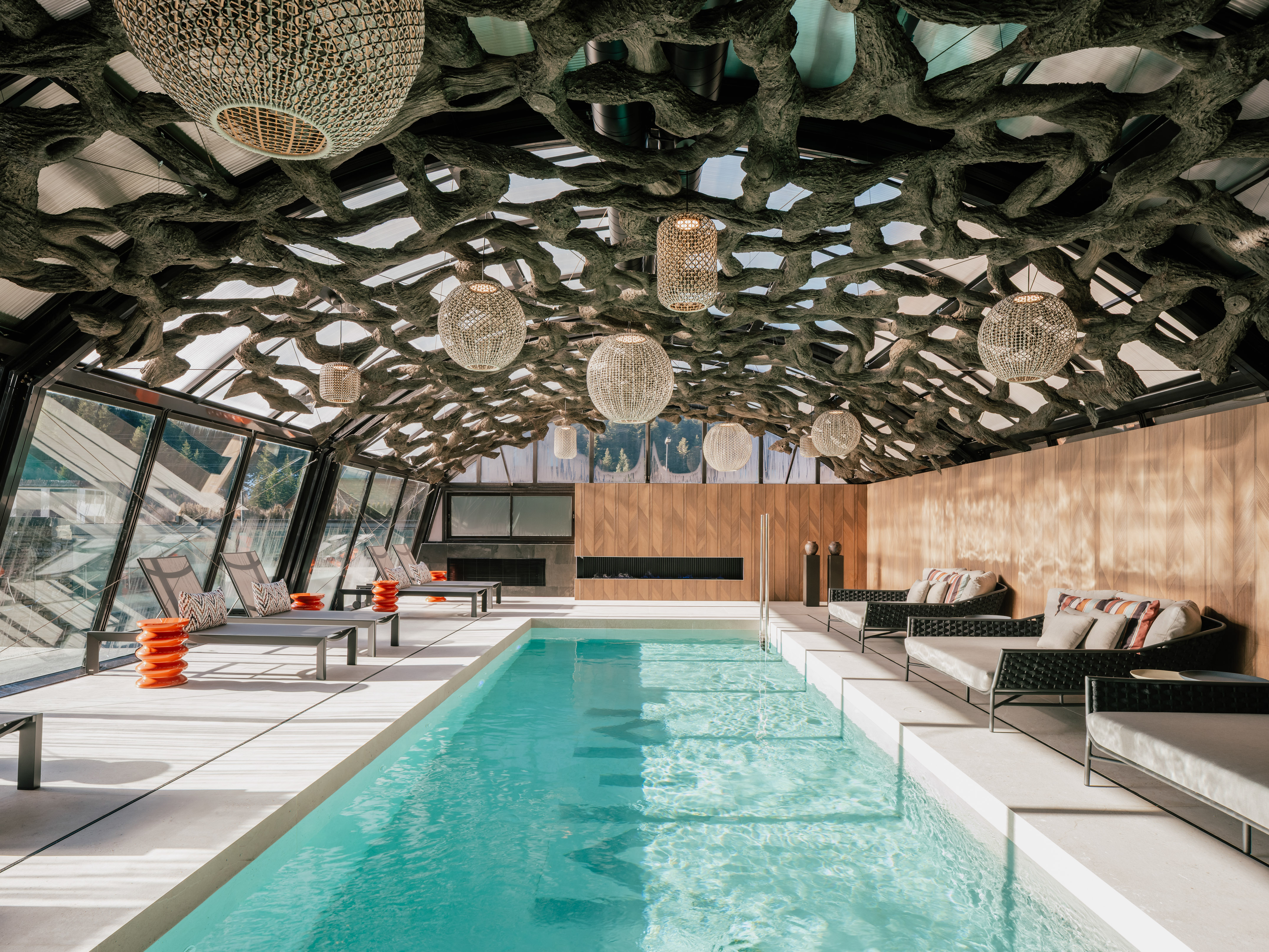 Luxury indoor pool with organic tree root ceiling and modern lounge seating.