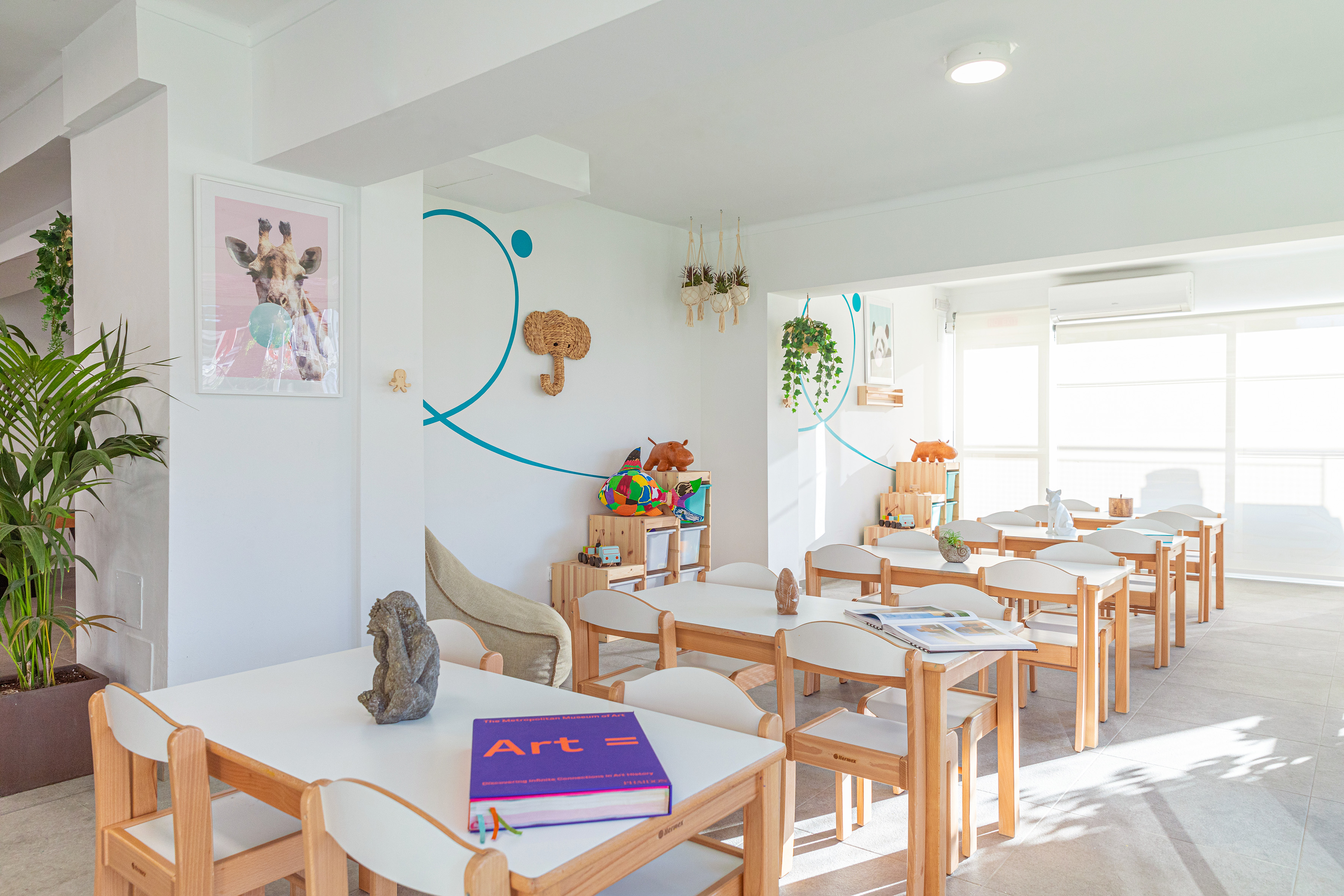 Bright children's classroom with small wooden tables, chairs, and playful decor.