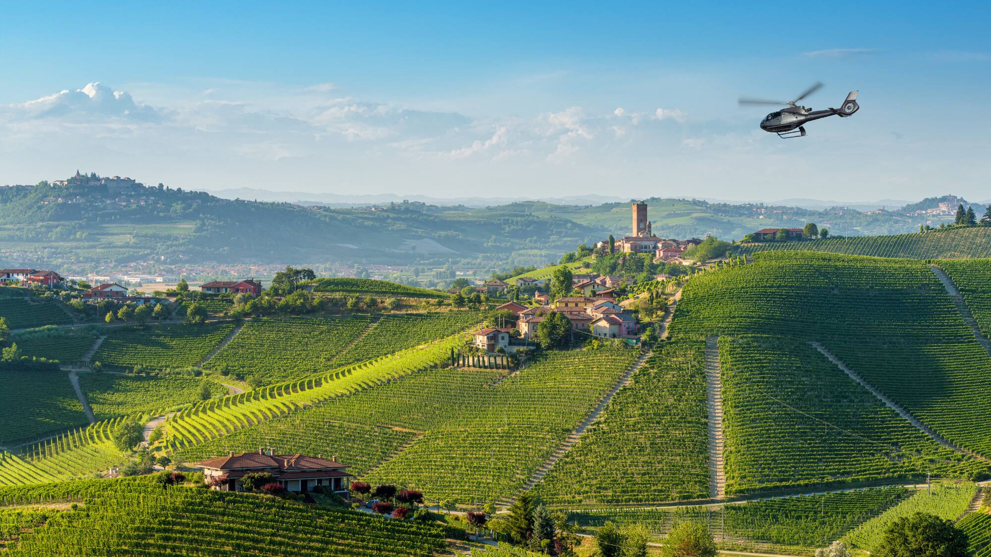 Helicopter above rolling Italian vineyards, village with ancient tower.