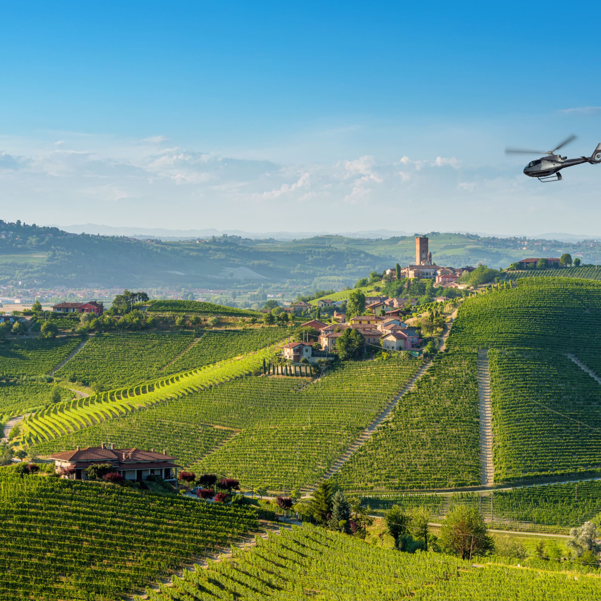 Helicopter flying over Italian vineyards, village, and historic tower.