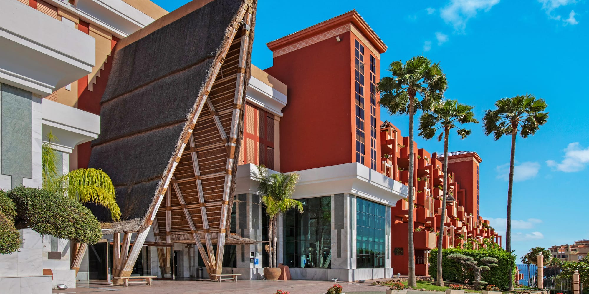 Red resort hotel with unique thatched roof entrance and palm trees.