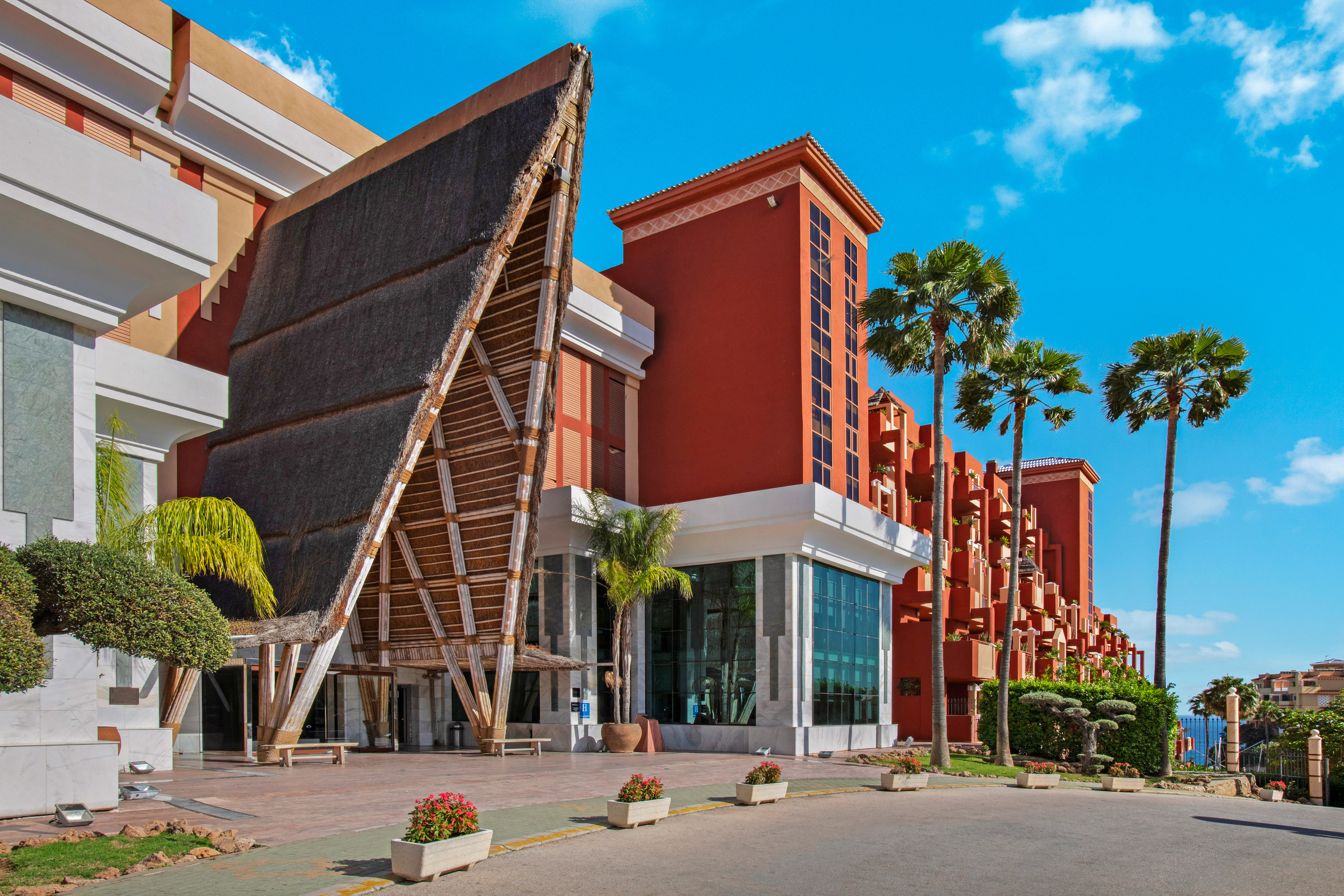Red resort hotel with unique thatched roof entrance and palm trees.