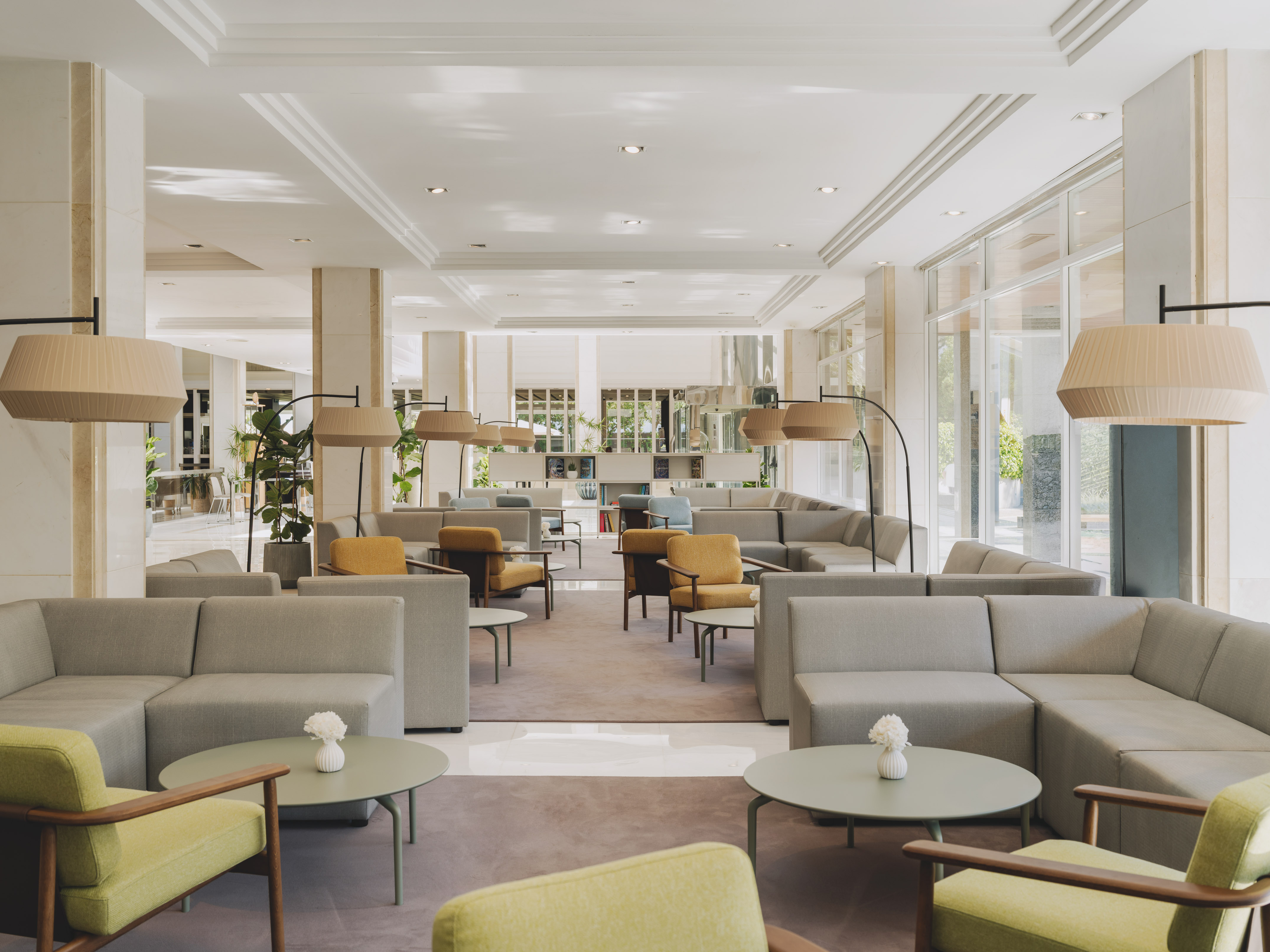 Modern hotel lounge with gray sofas, green & mustard armchairs, and sleek lamps.
