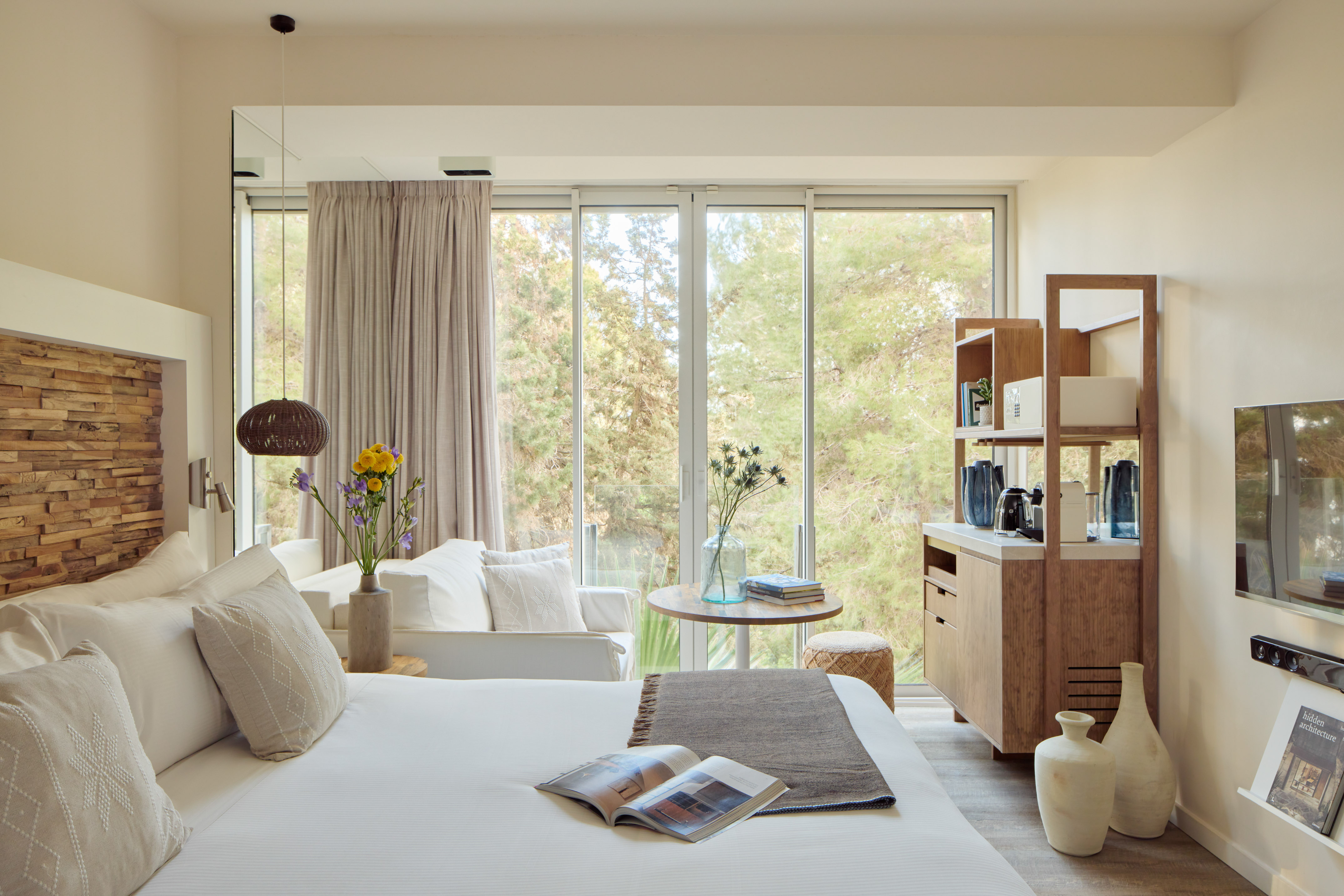 Cozy modern hotel bedroom with natural light, forest view, and stylish wooden decor.