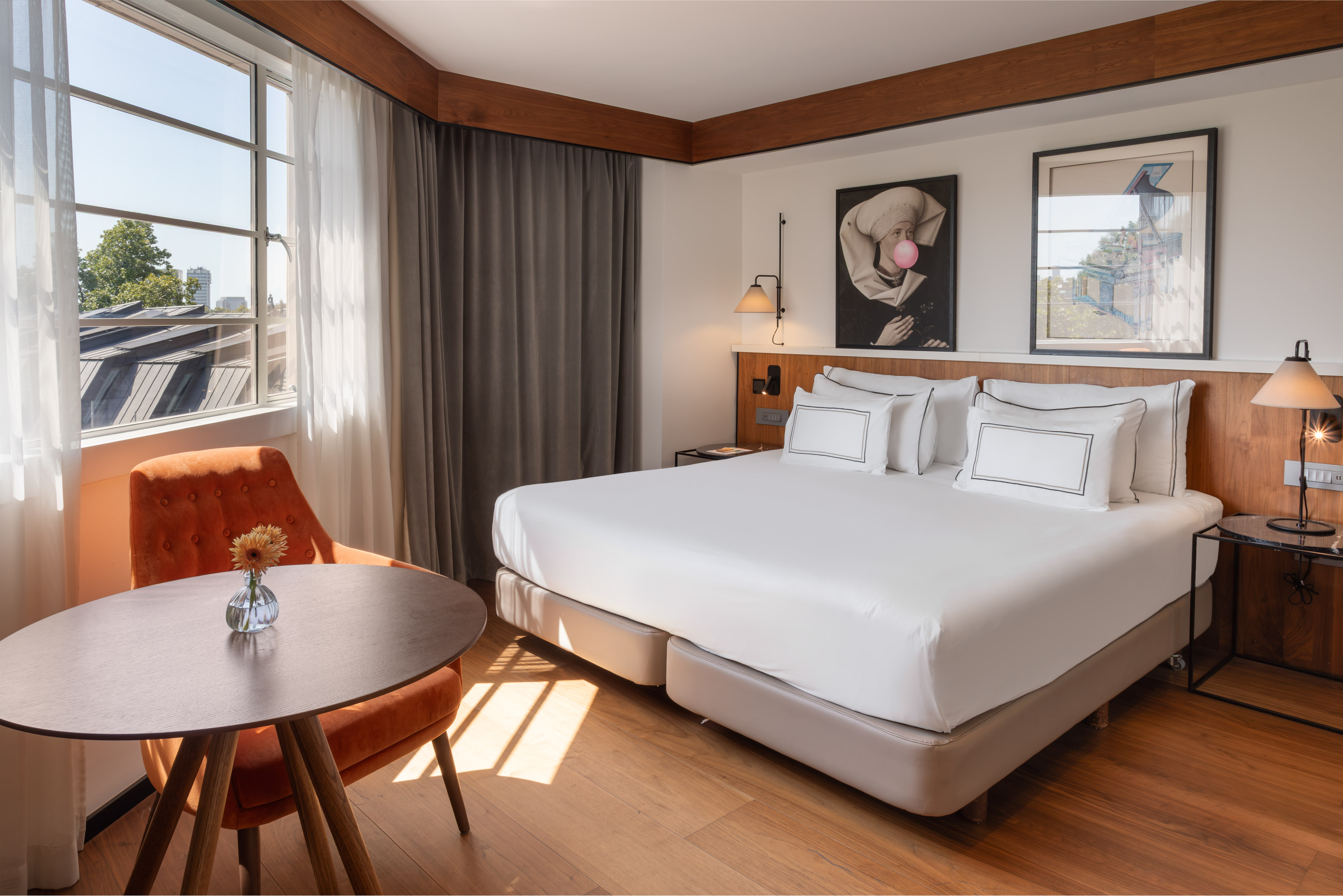 Bright hotel bedroom with large bed, city view, and cozy seating.