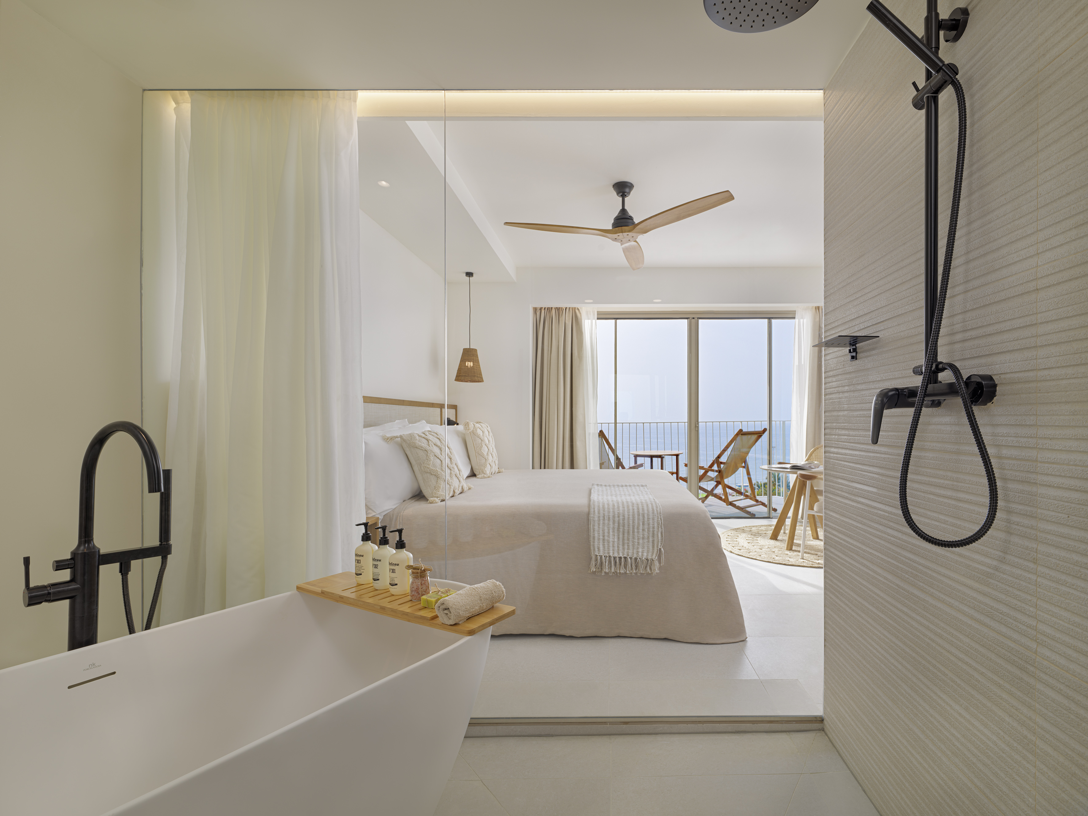 Luxury suite: modern bedroom with freestanding tub, ocean view balcony.