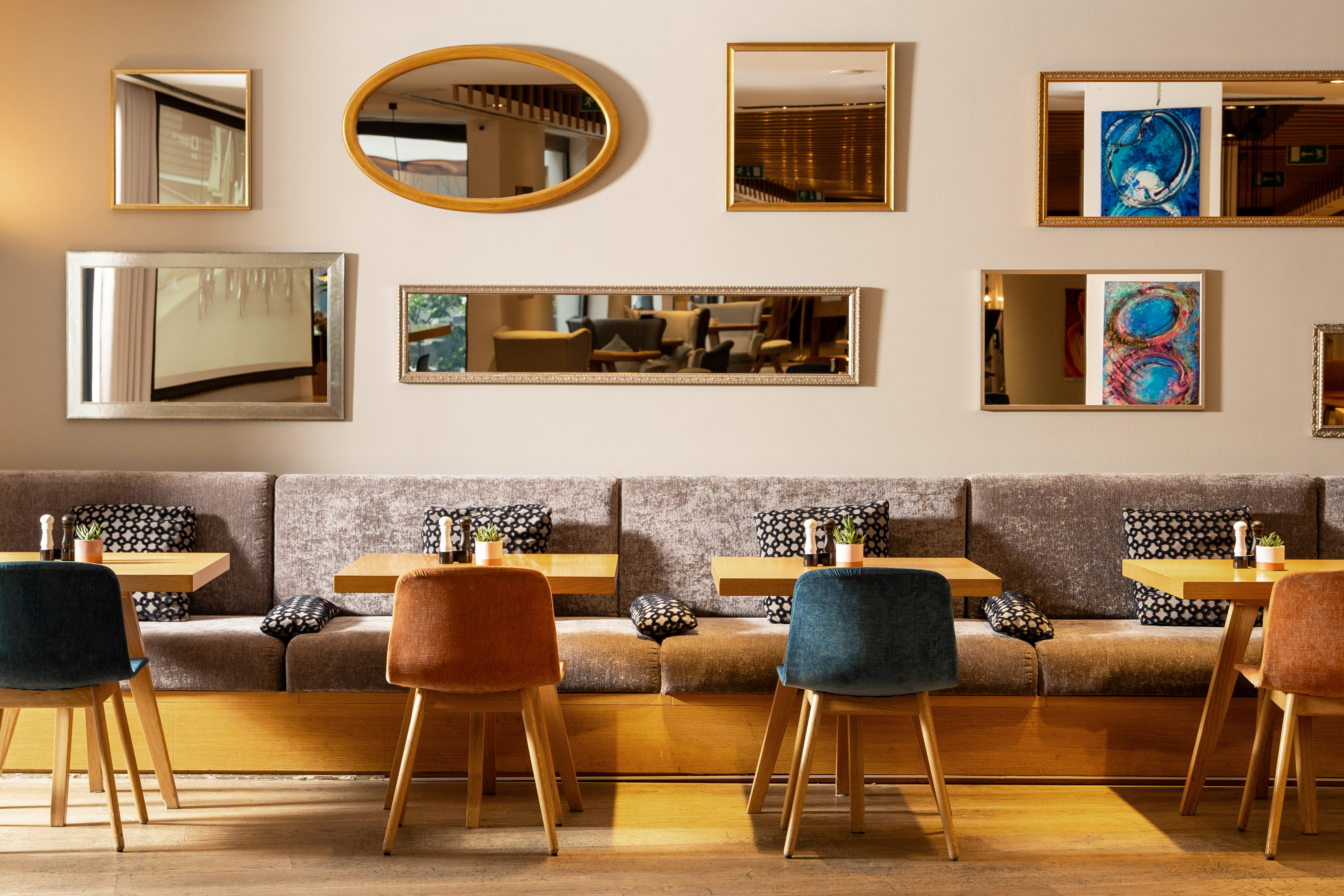 Cafe dining area with decorative mirrors, upholstered booth seating, and wooden tables.