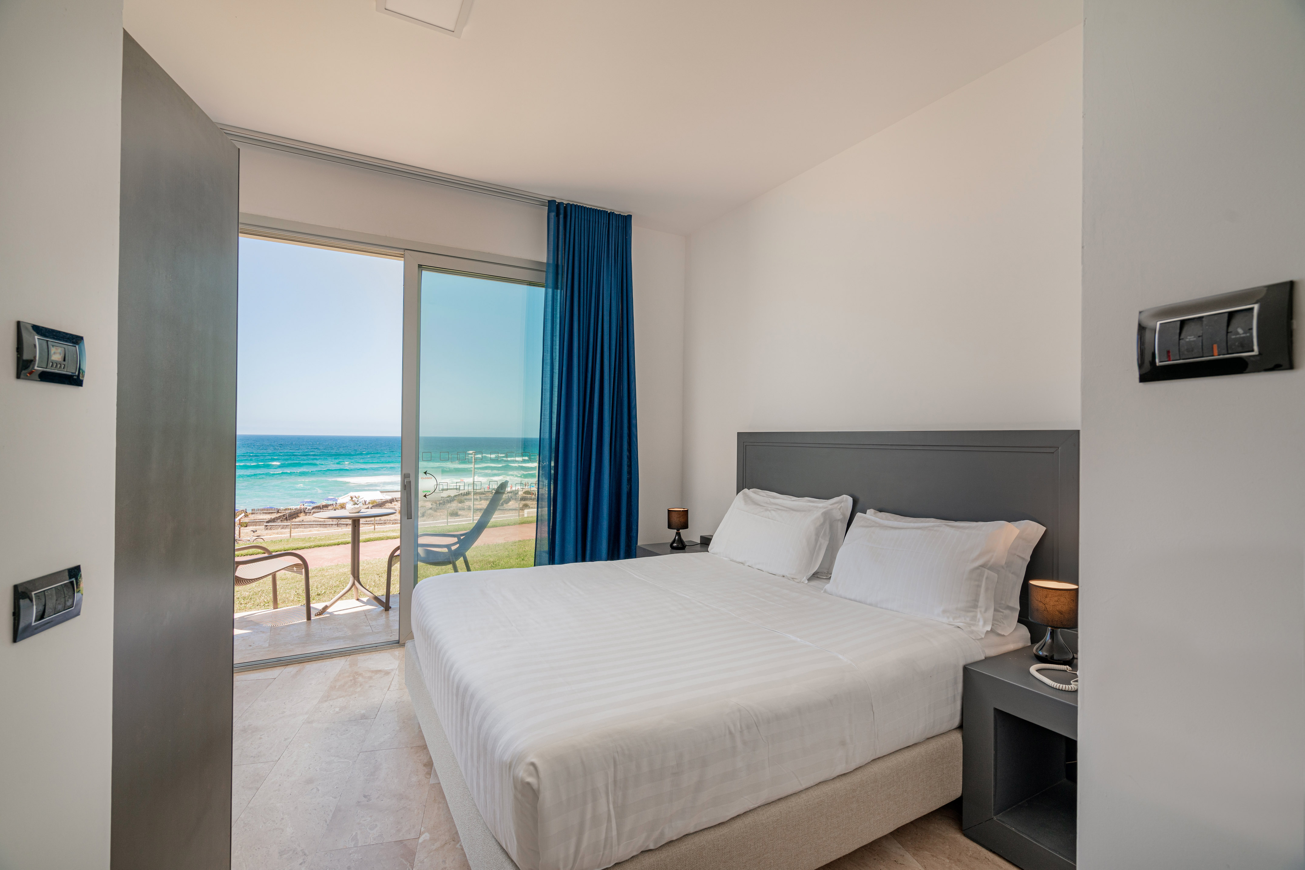 Modern beachfront bedroom with sea view balcony and white bed.