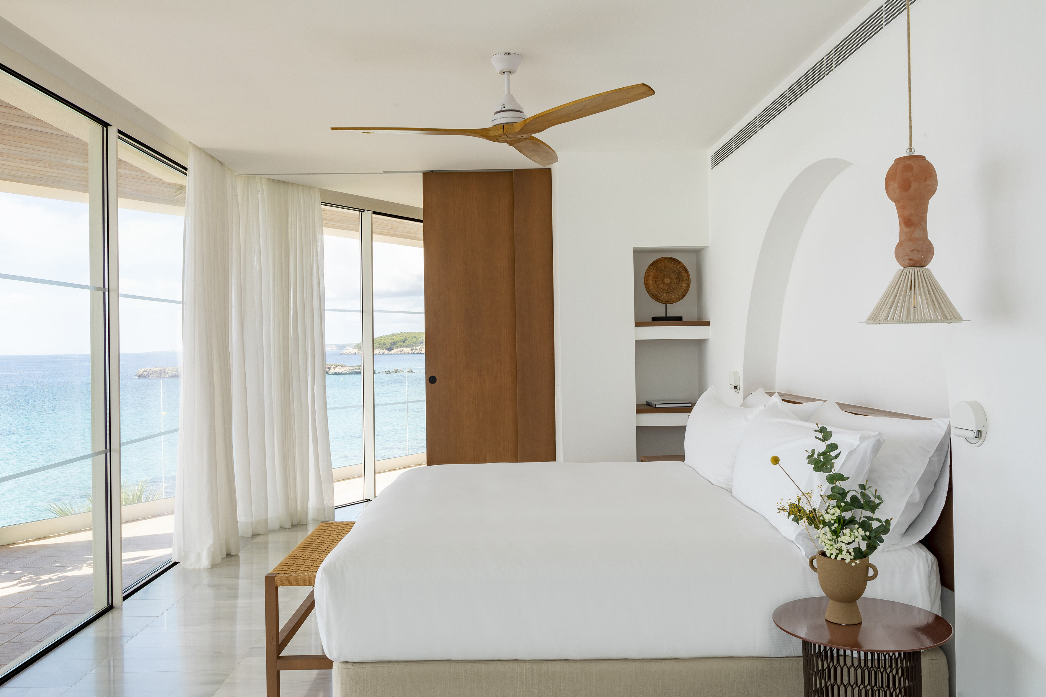 Coastal bedroom with expansive sea view, white decor, and wooden accents.