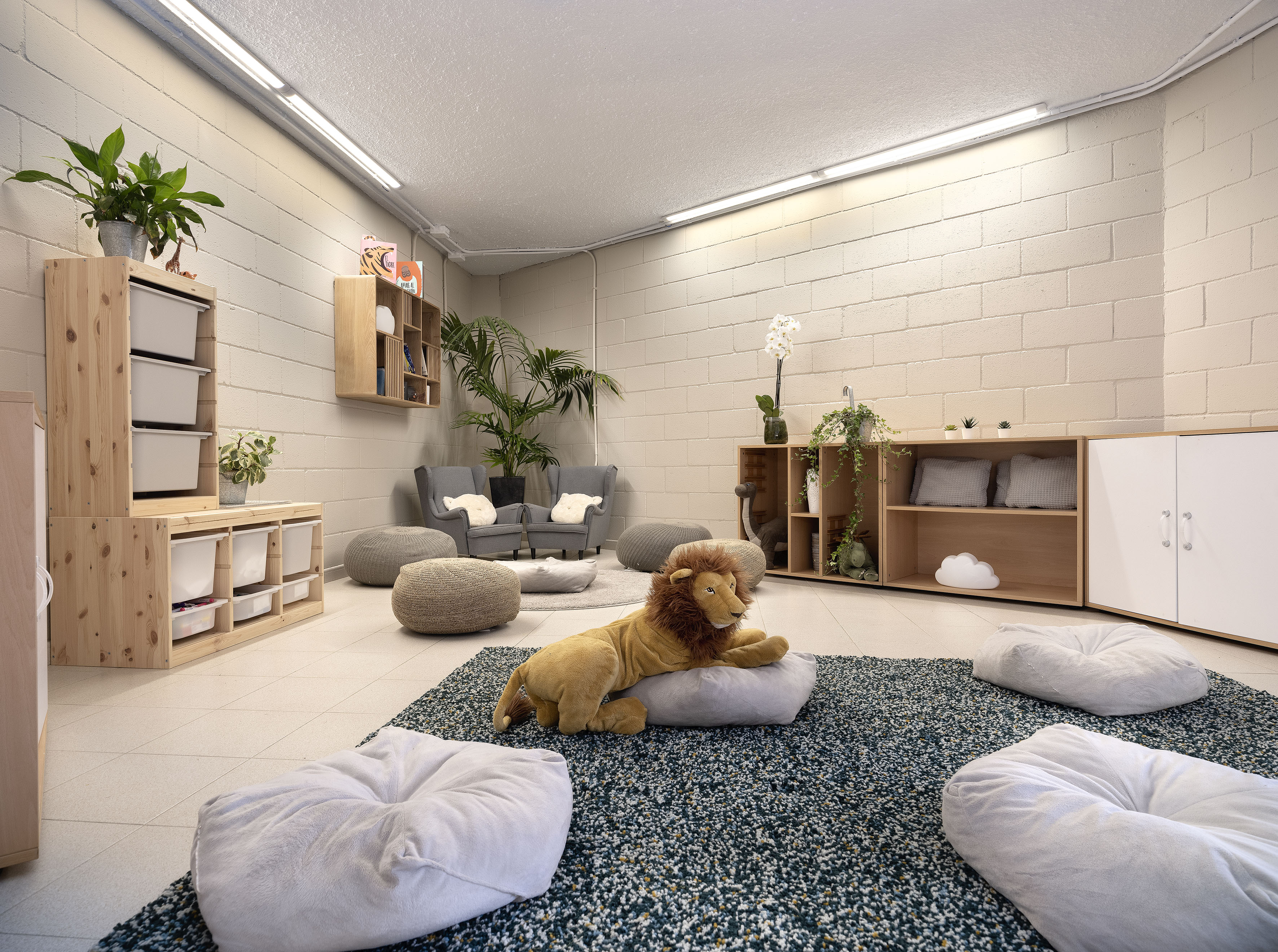 Cozy kids' lounge area with a plush lion, bean bags, wooden storage, and plants.