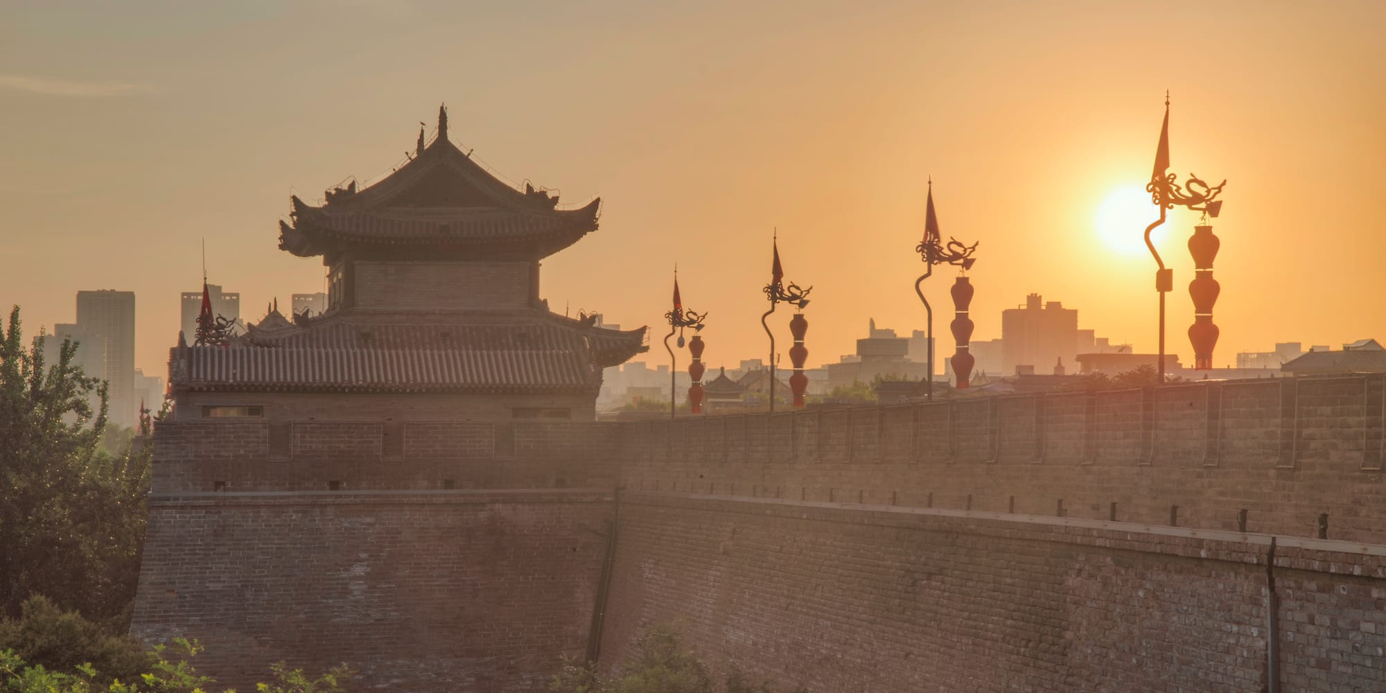 a wall with a building and a tower with a sunset