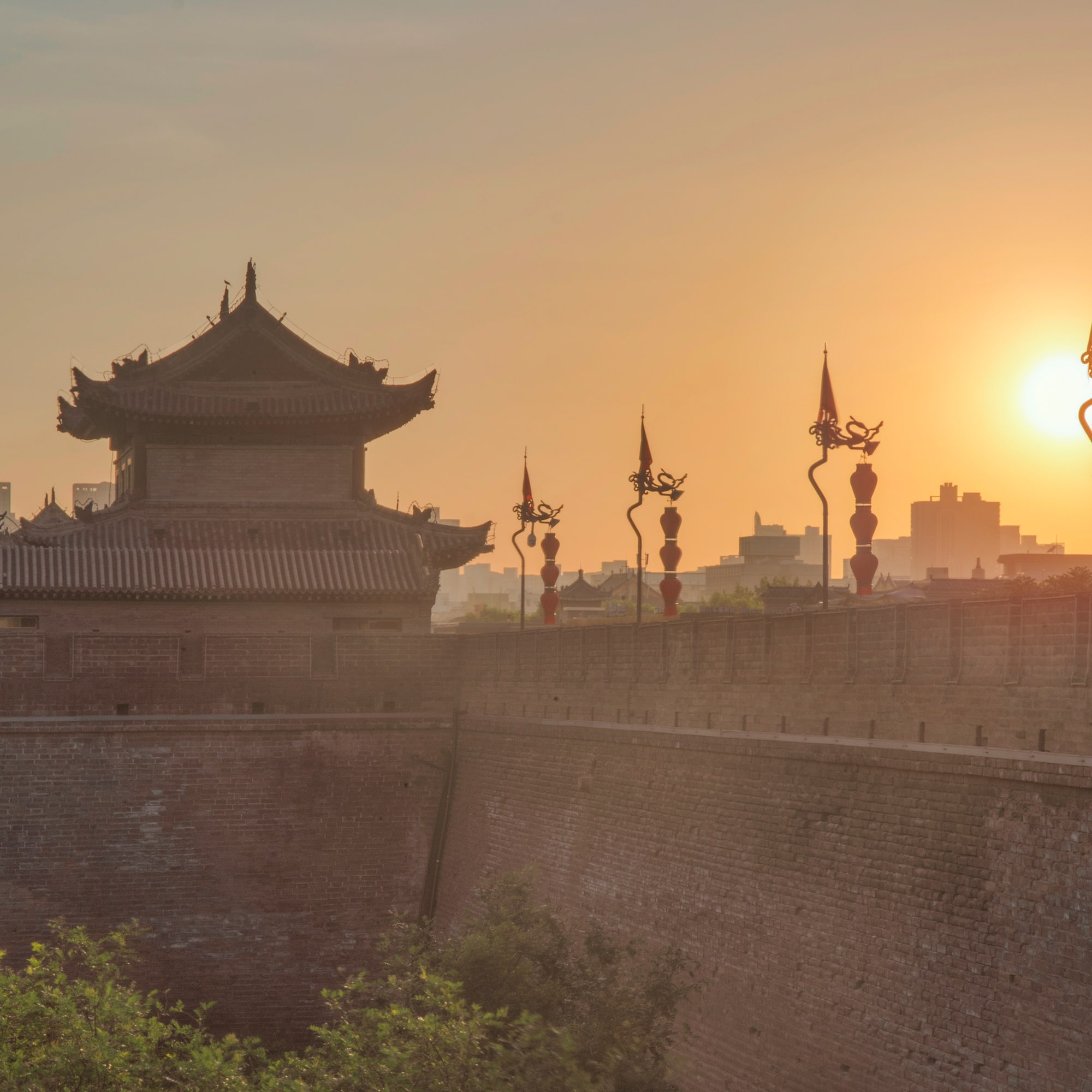 a wall with a building and a tower with a sunset