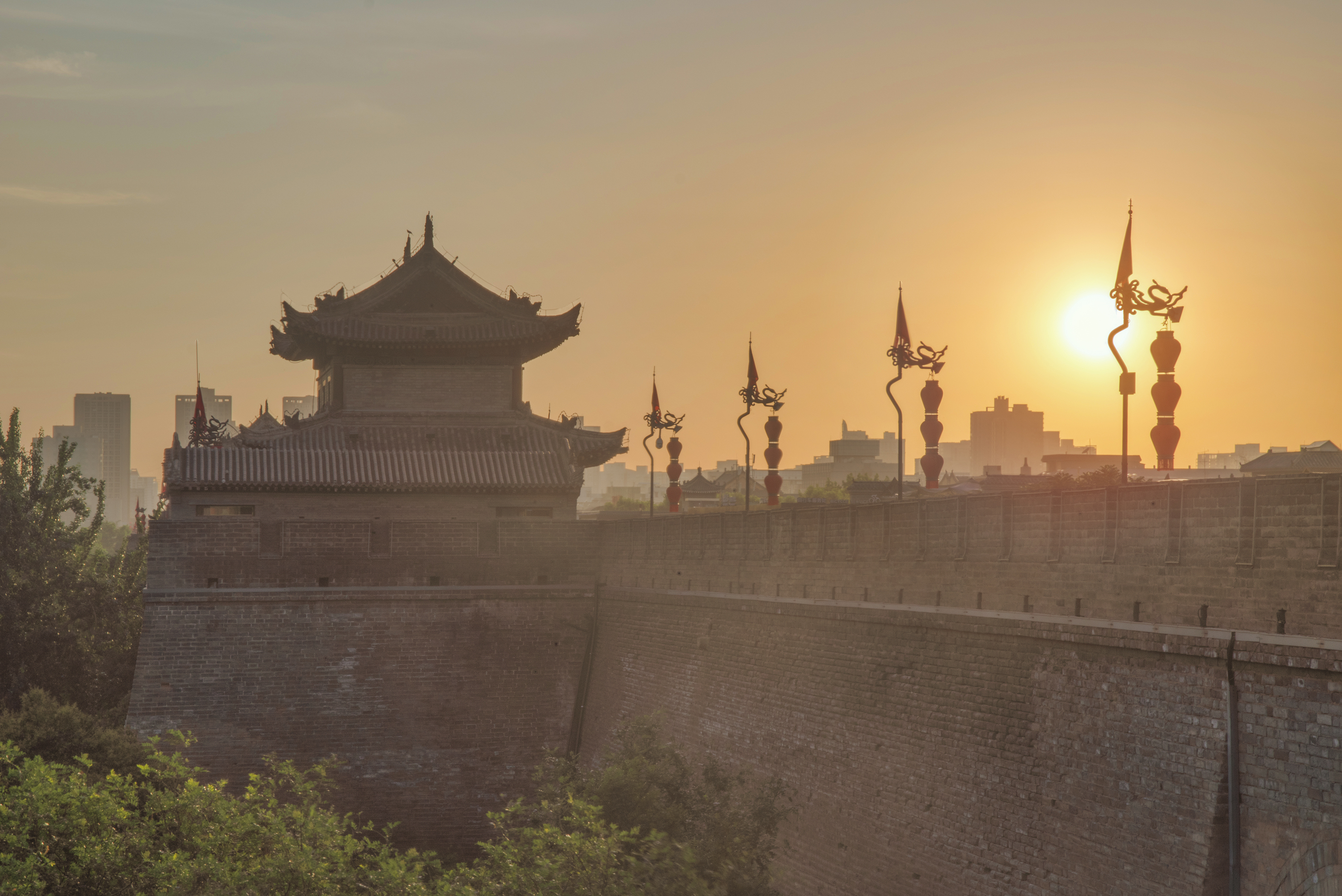 a wall with a building and a tower with a sunset