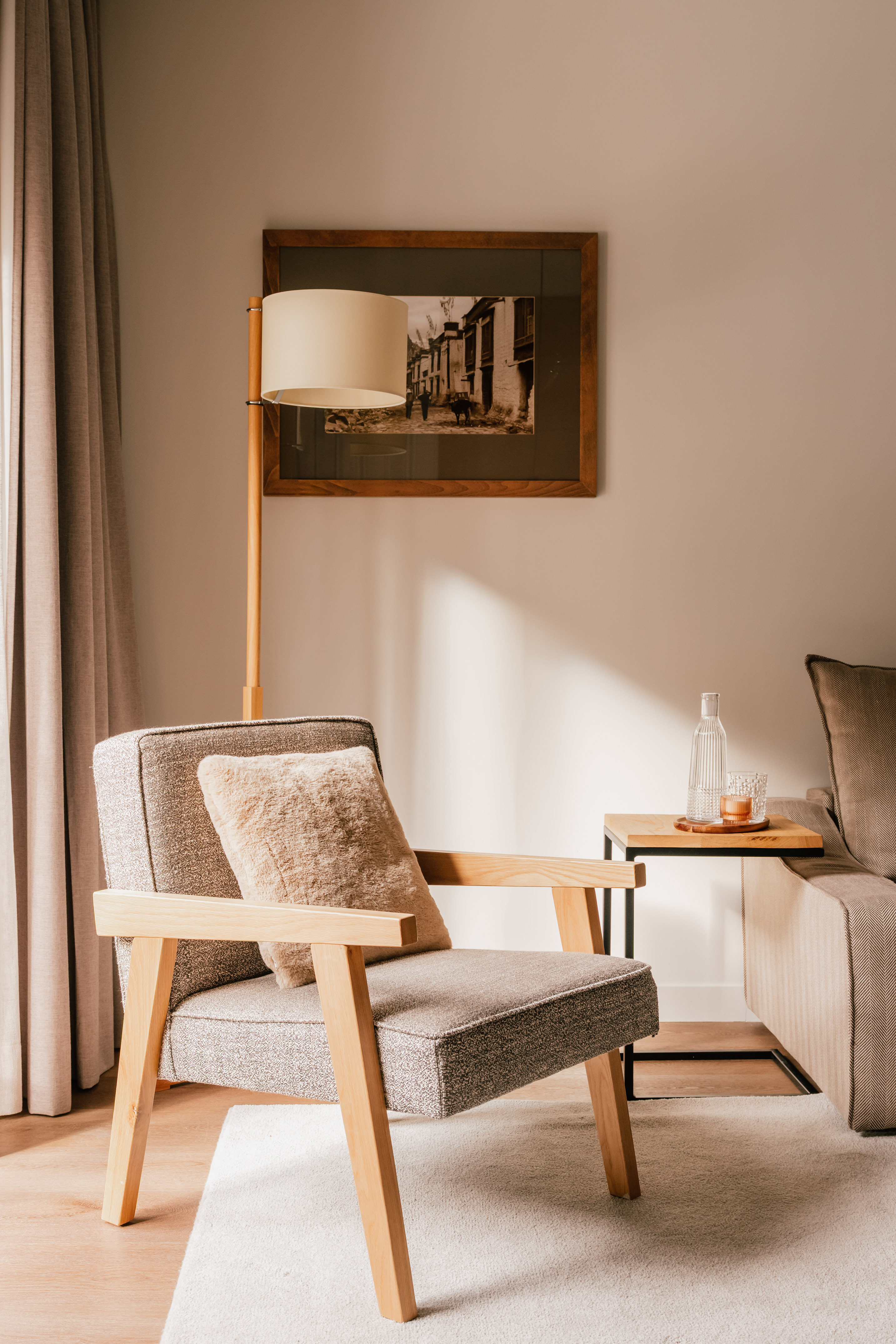 Modern living room with grey armchair, wooden floor lamp, side table, framed art.