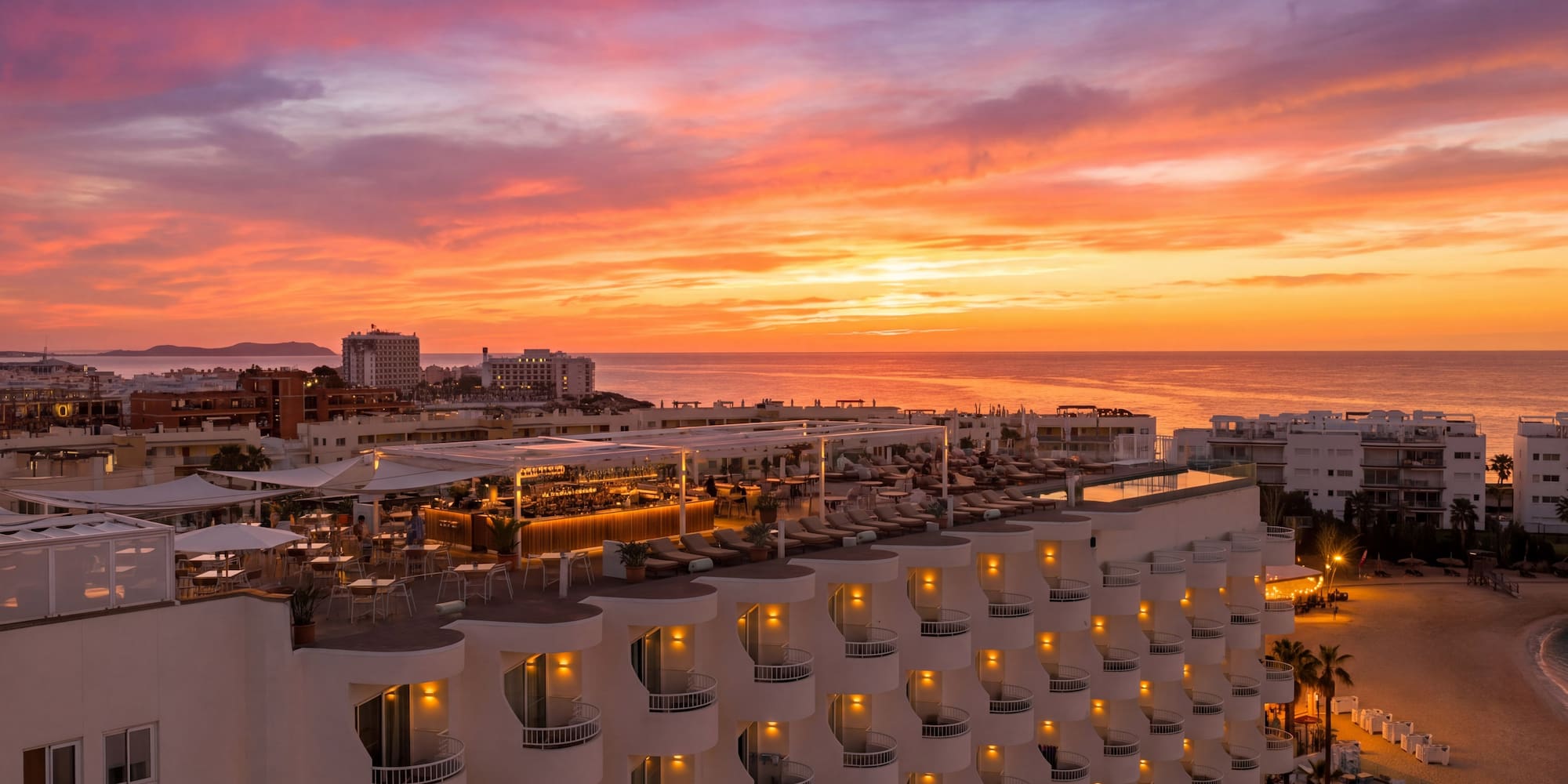 Vibrant sunset over resort hotel rooftop bar, ocean, and beach.