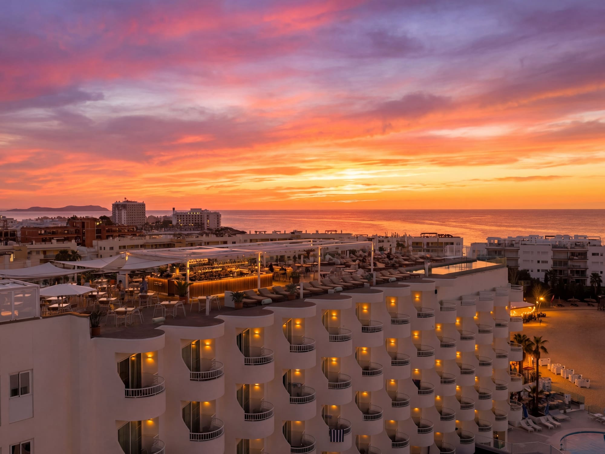 Vibrant sunset over resort hotel rooftop bar, ocean, and beach.