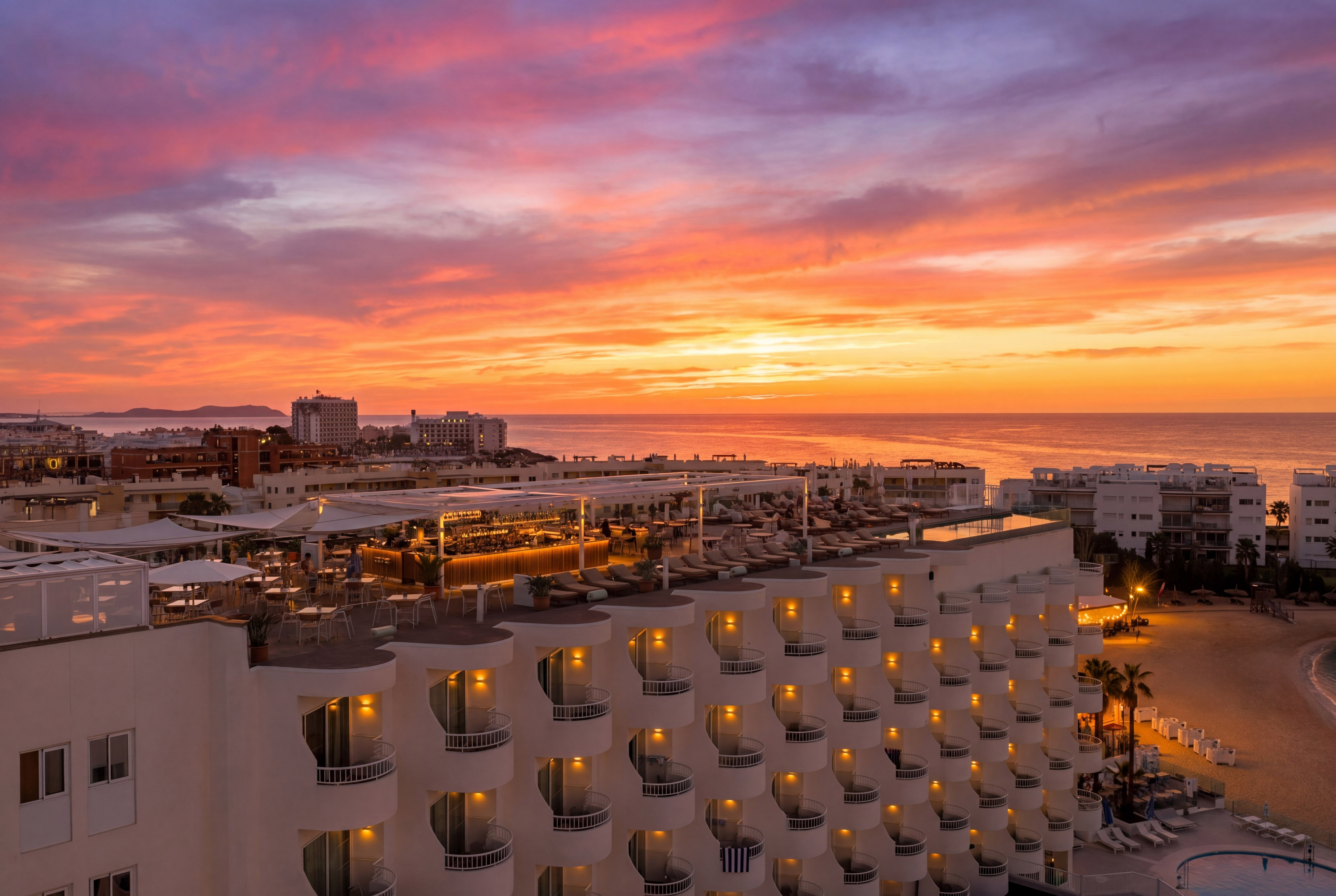 Vibrant sunset over resort hotel rooftop bar, ocean, and beach.