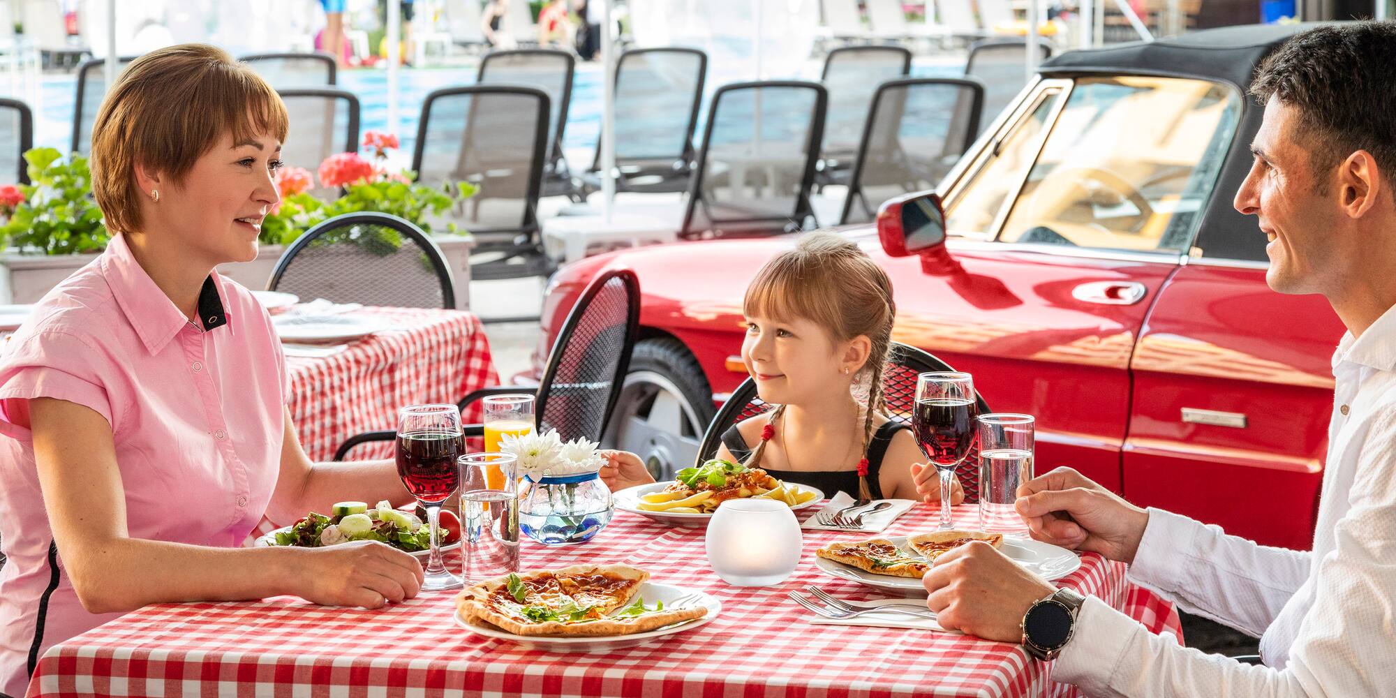 a man and woman sitting at a table with a girl eating pizza