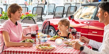 a man and woman sitting at a table with a girl eating pizza