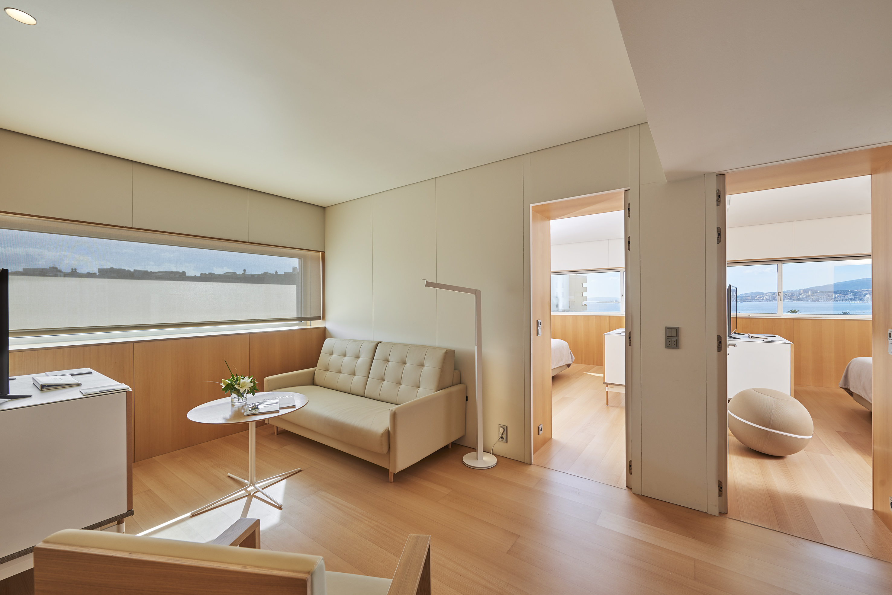 Modern hotel suite living room with sea view, sofa, and hardwood floor.