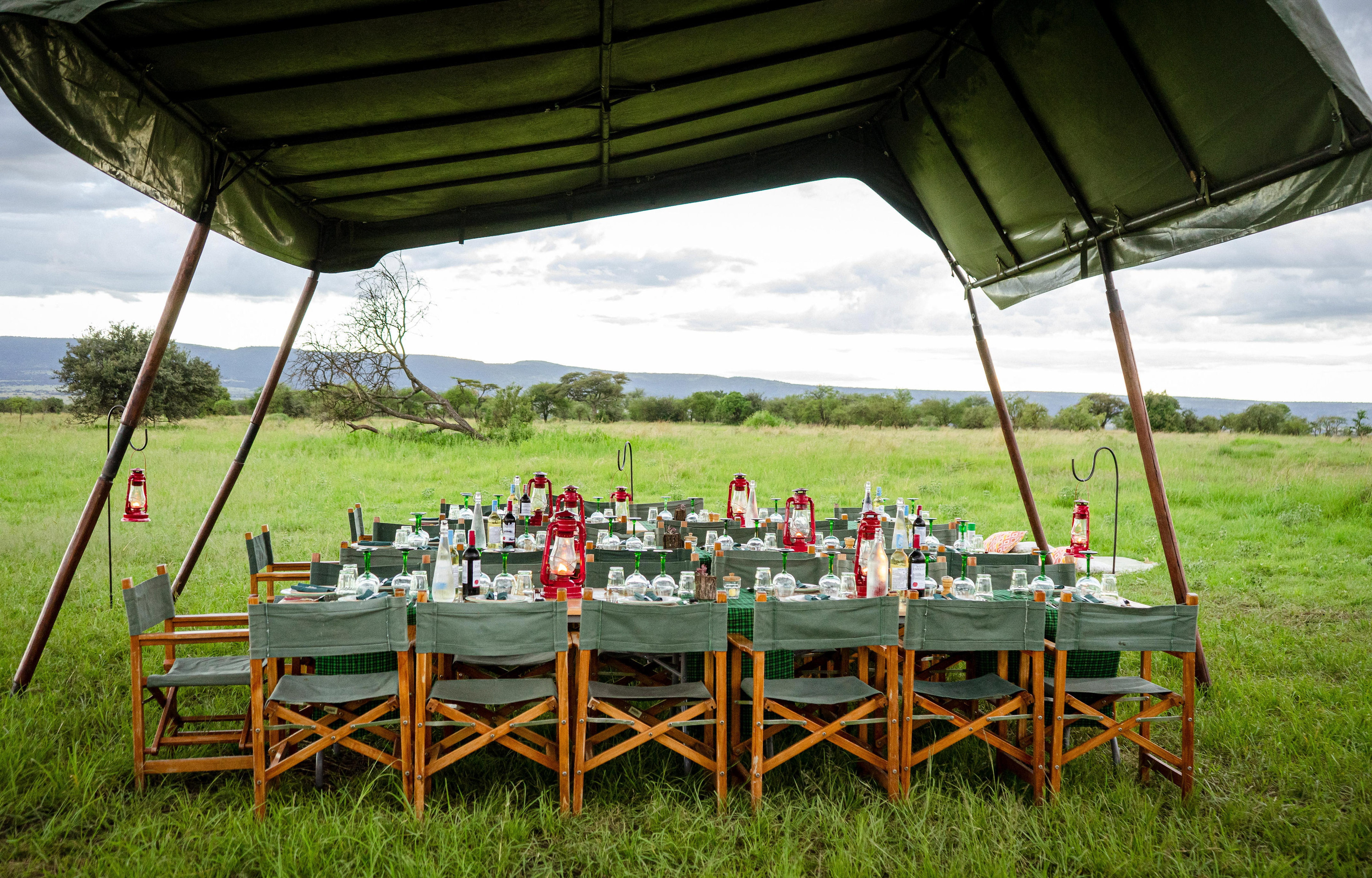 Bush dinner table with green chairs and red lanterns under a safari tent.