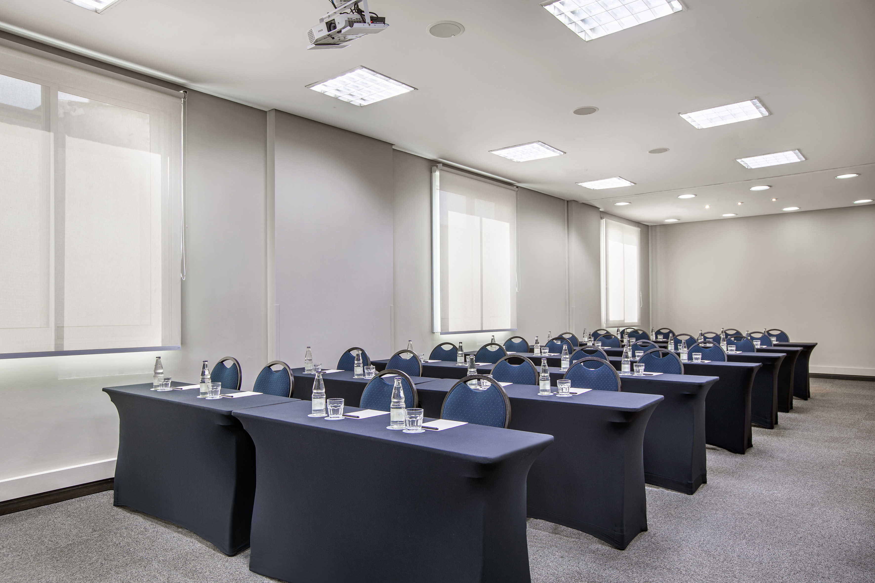 Conference room with rows of tables, blue chairs, projector, and water.