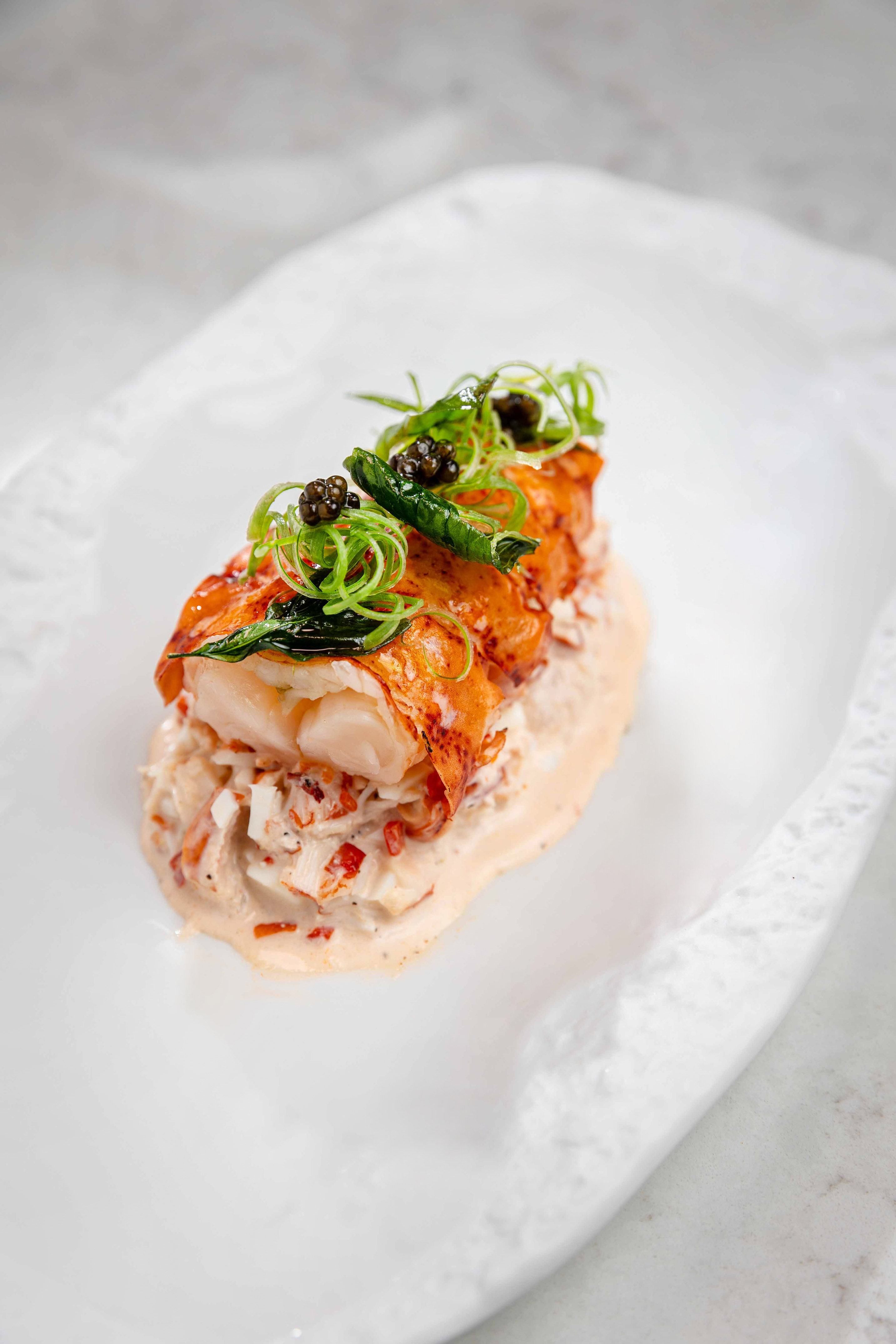 Cooked lobster tail on creamy lobster salad, garnished with black caviar and chives.