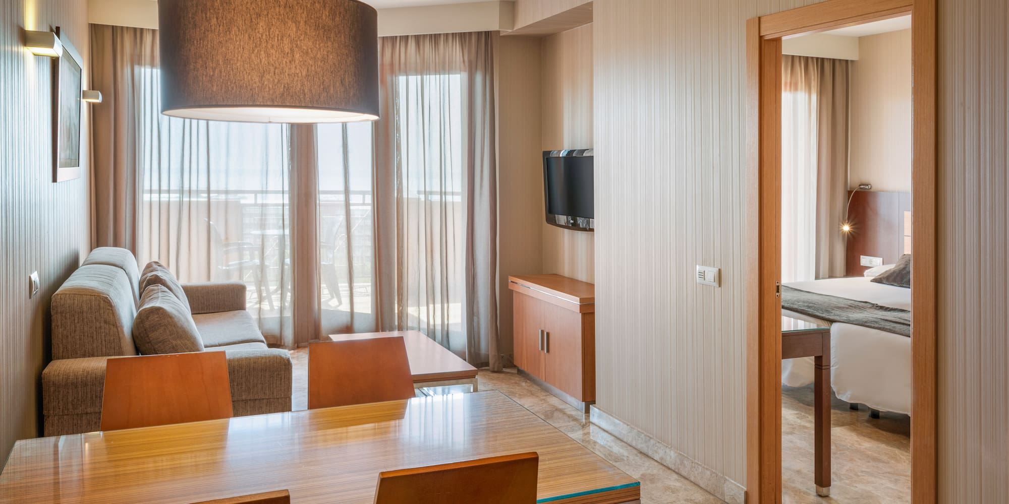 Modern hotel suite with living room, dining area, and doorway to a bedroom.