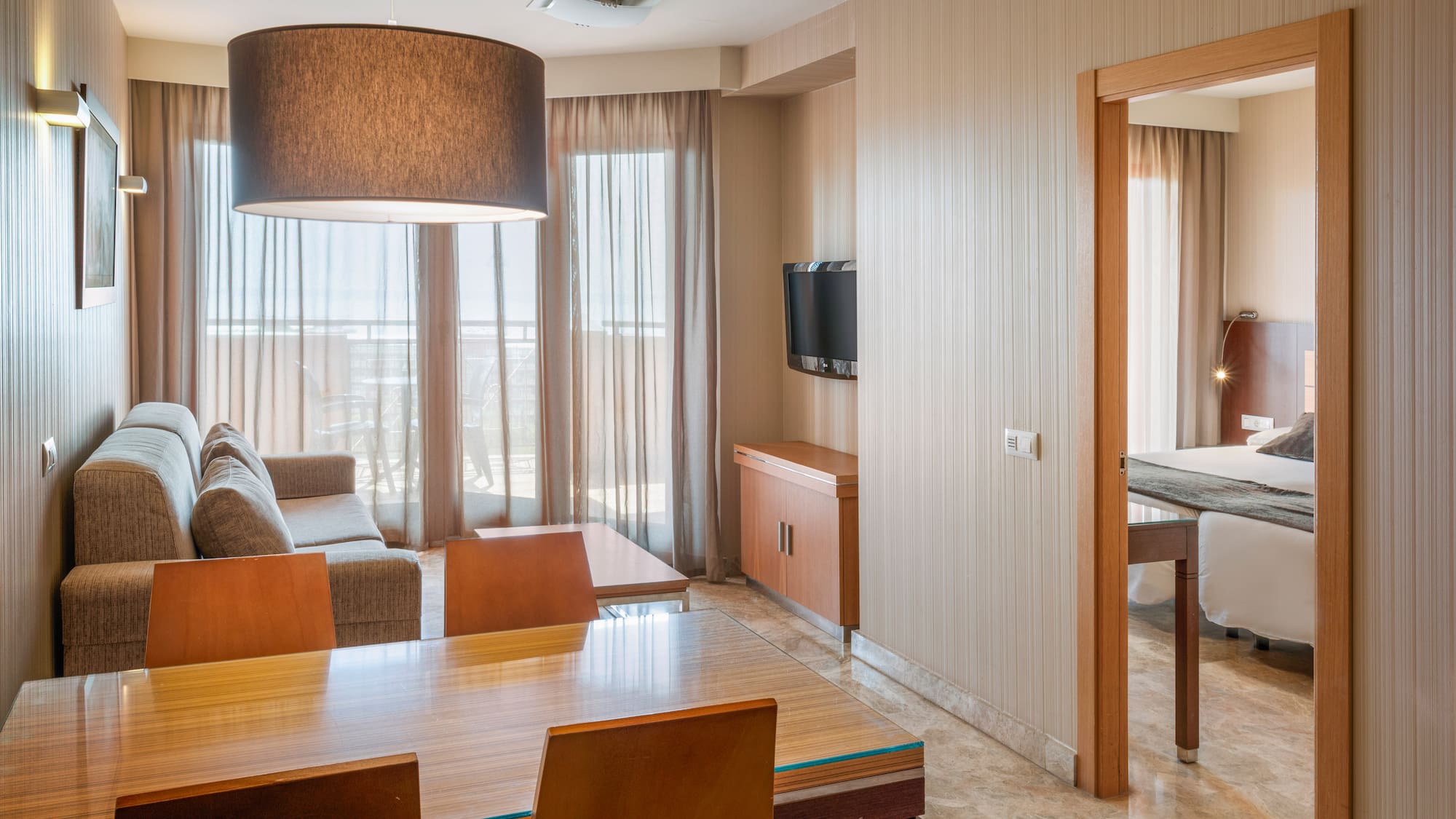 Modern hotel apartment living and dining area with bedroom view, neutral decor.