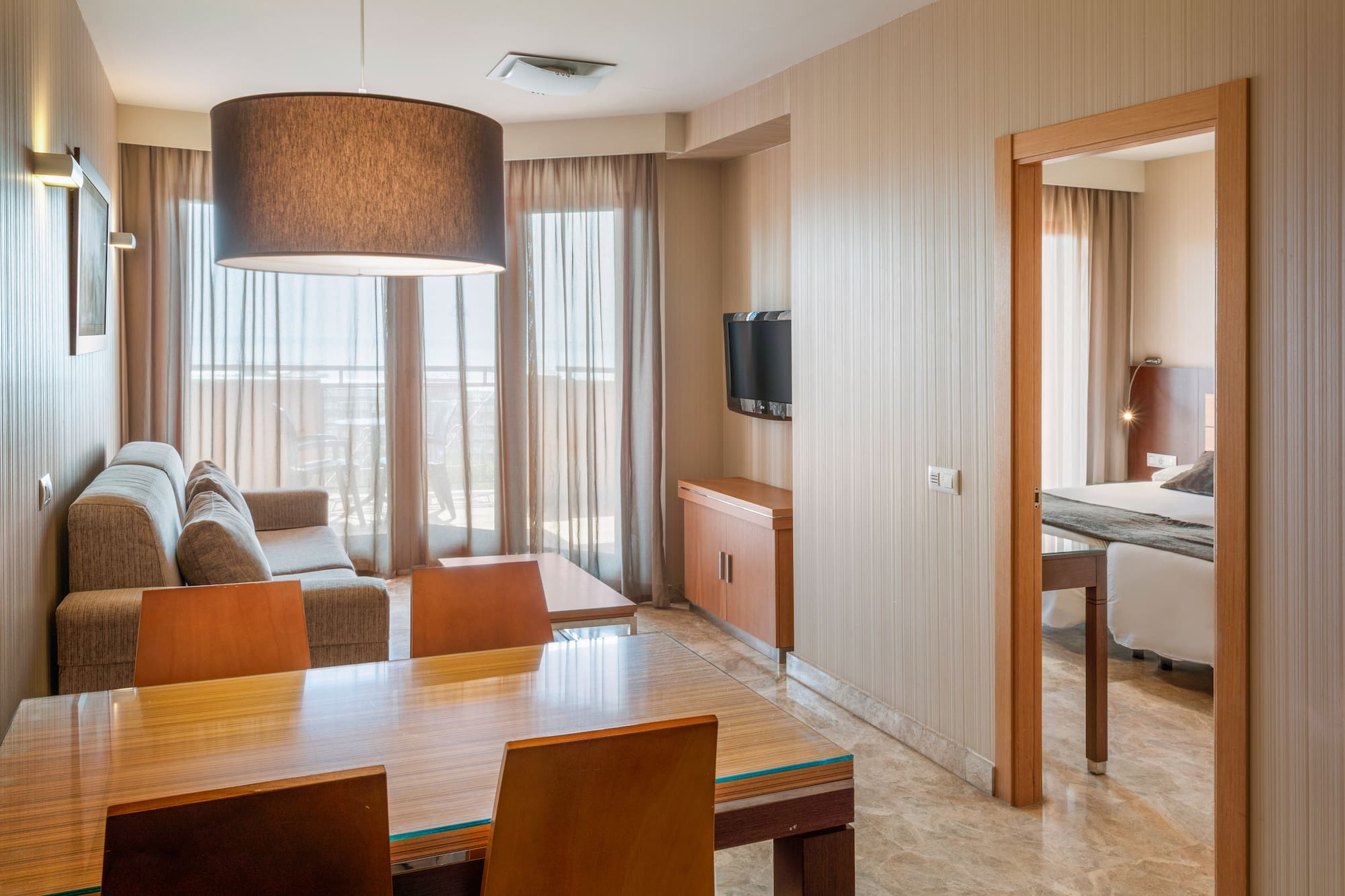 Hotel suite living room sofa, dining table, balcony, and bedroom view.