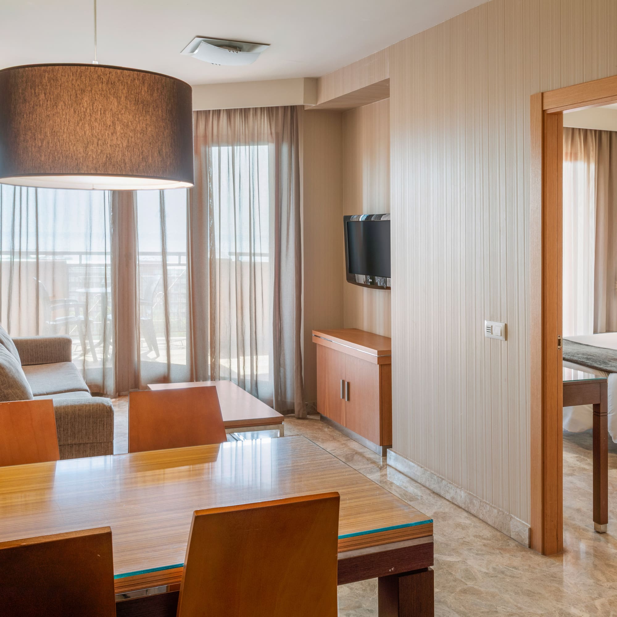 Modern hotel suite with living room, dining area, and doorway to a bedroom.
