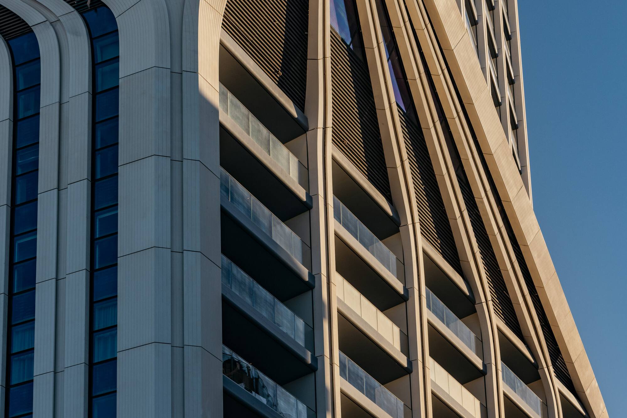Modern skyscraper with wavy arched facade, ribbed concrete, and glass balconies.