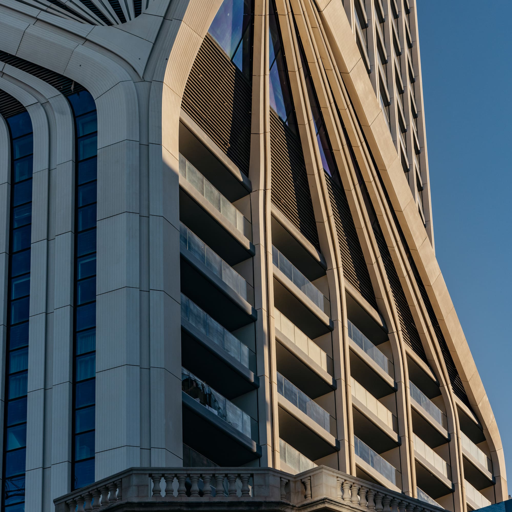 Curved modern building facade with balconies, above a traditional stone base.