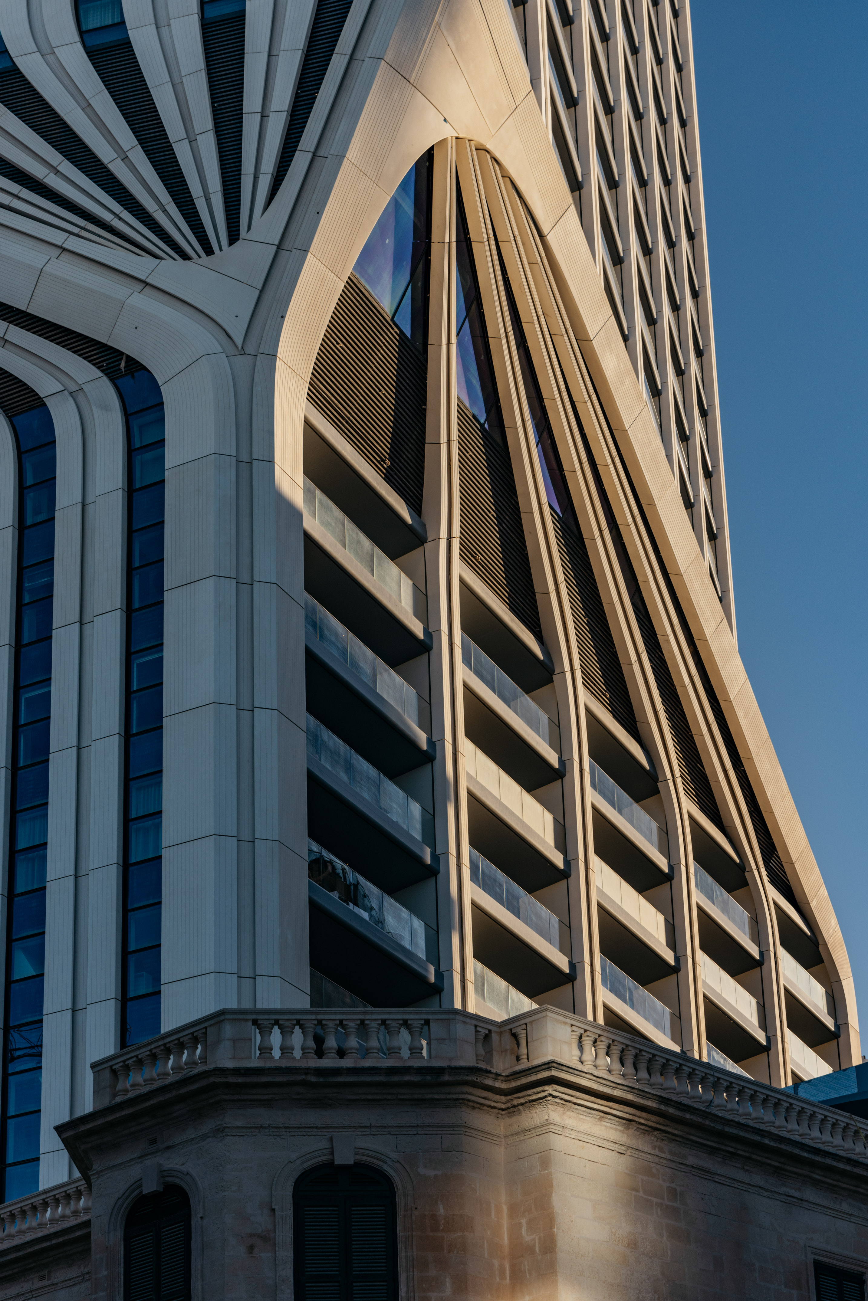Curved modern building facade with balconies, above a traditional stone base.