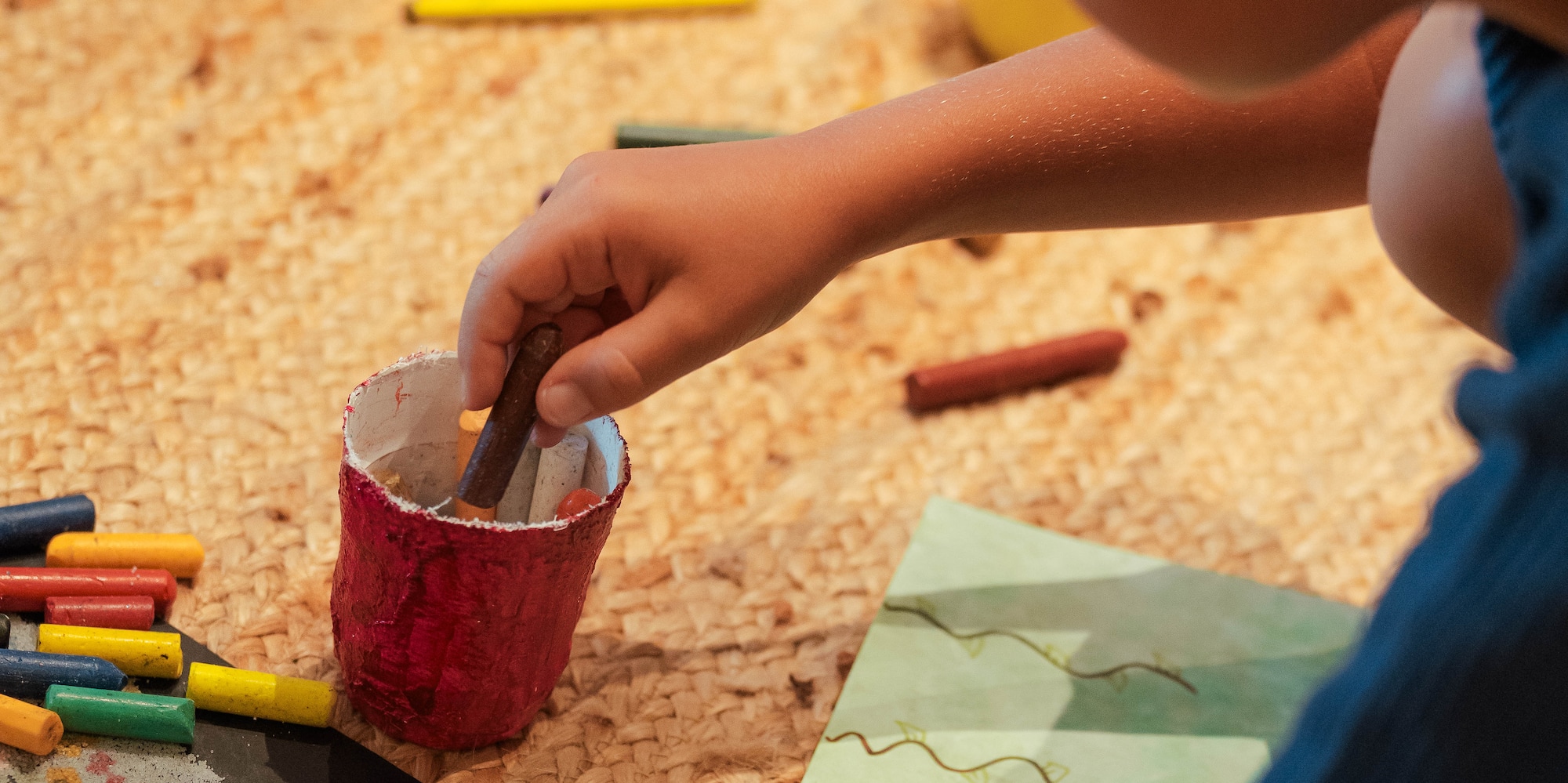 Niño dibujando con crayones de cera sobre una alfombra, creatividad infantil.