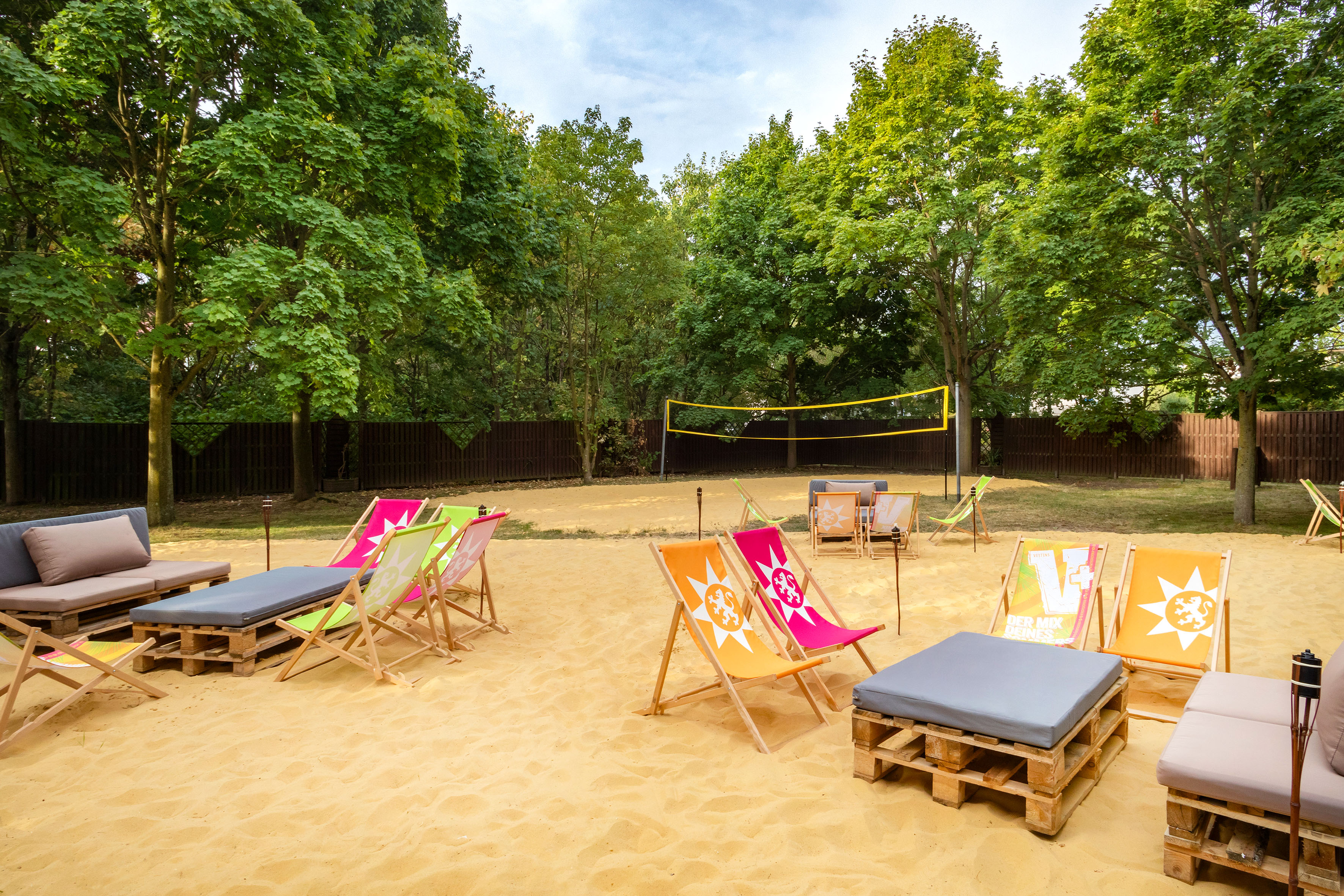 Outdoor beach volleyball court with colorful deck chairs and pallet seating.