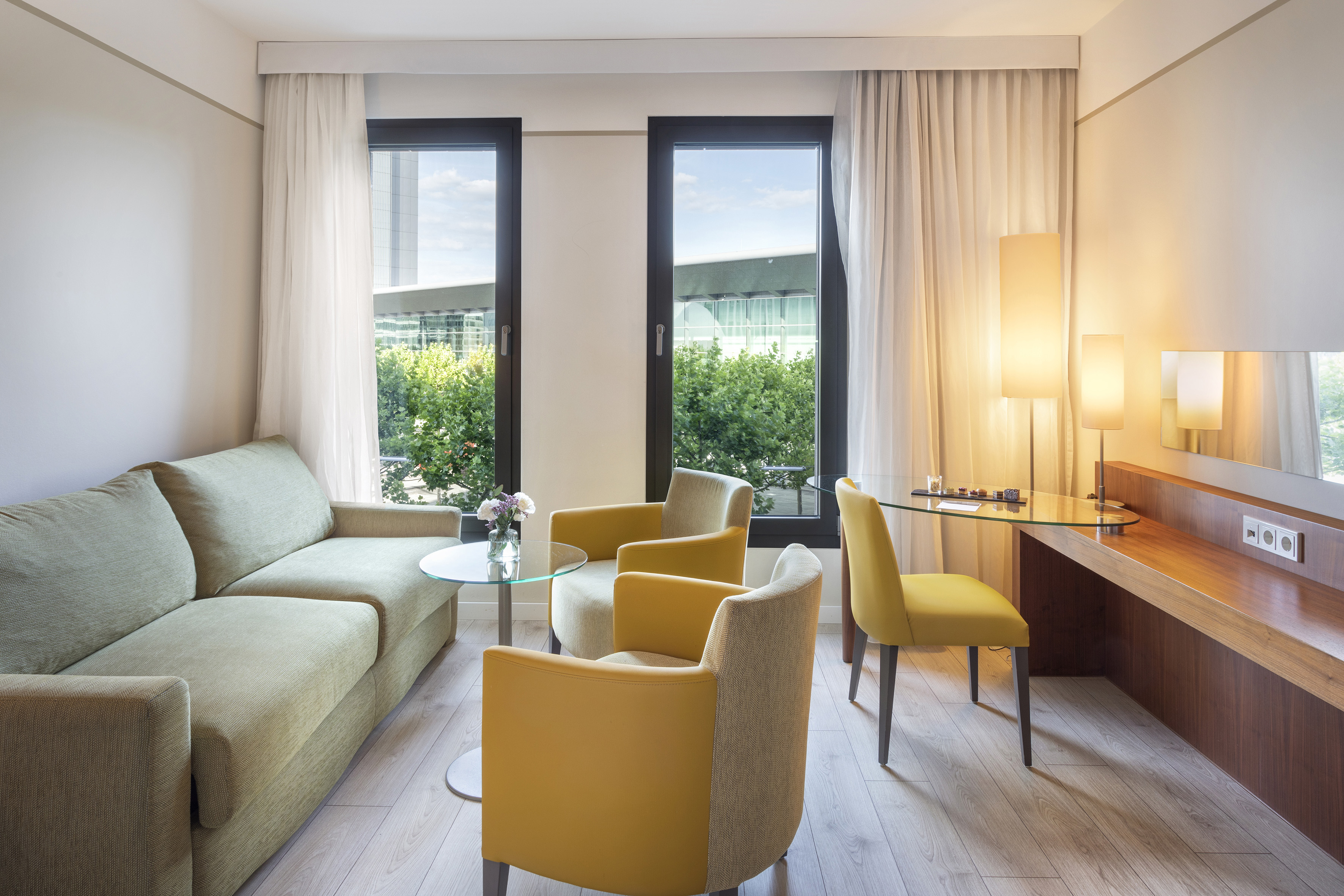 Cozy hotel room living area with green sofa, yellow armchairs, and bright windows.