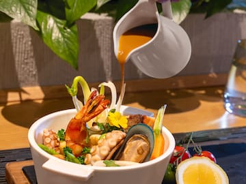 a bowl of seafood with sauce being poured into it