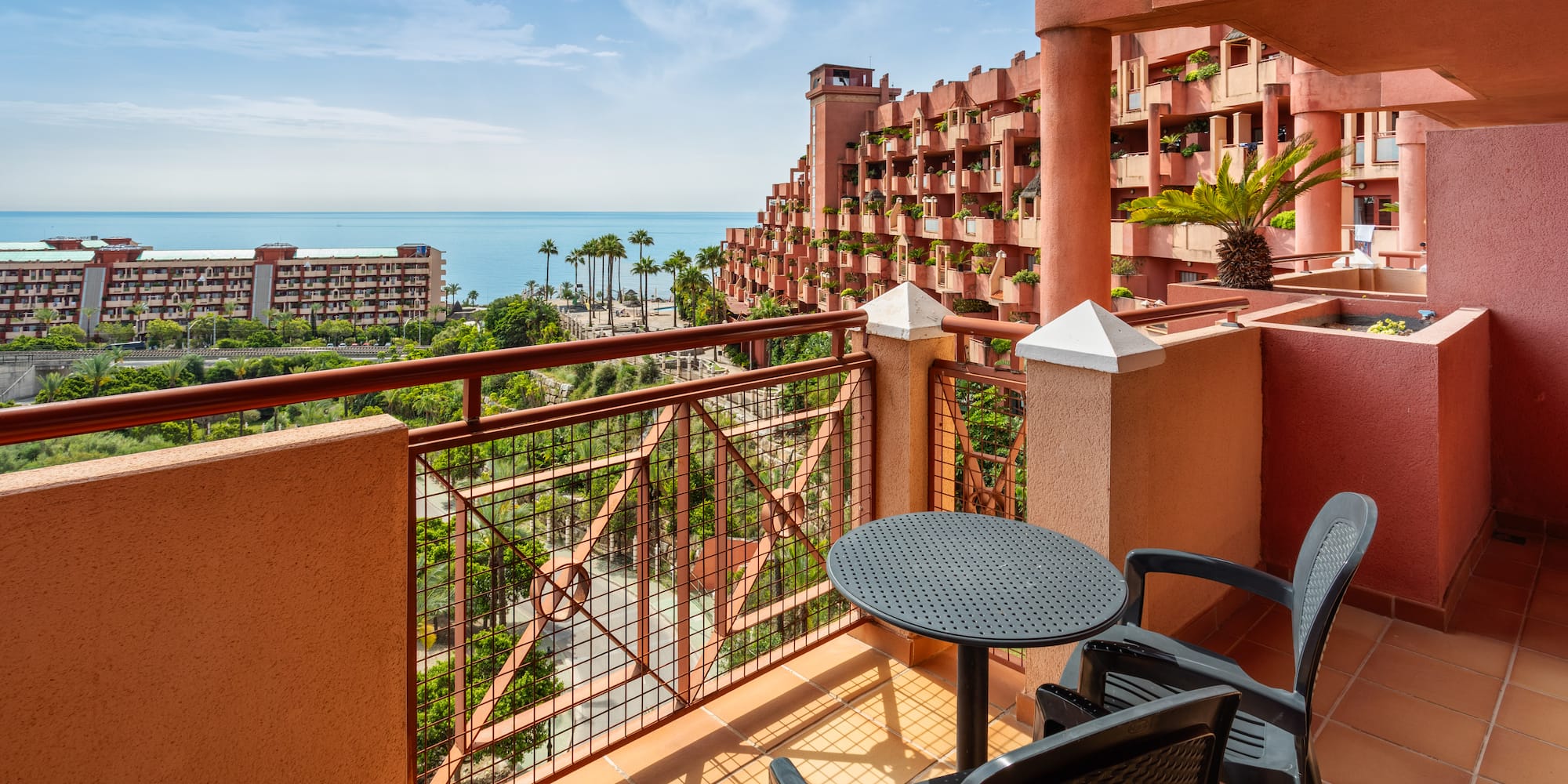 Hotel balcony overlooking Mediterranean sea, unique red resort, palm trees.